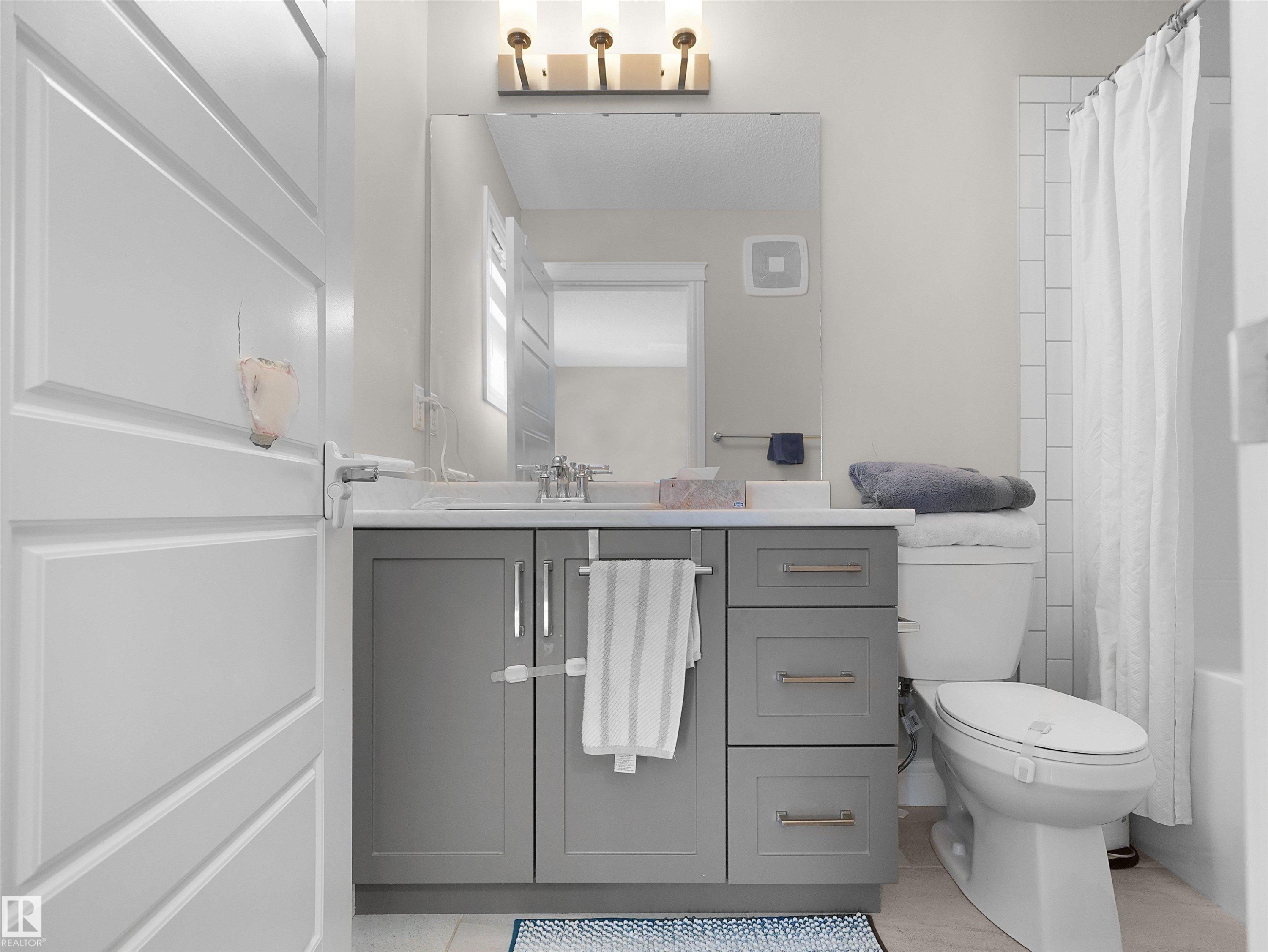 Bathroom featuring a gray vanity with a light-toned countertop, a large mirror, a toilet, and subway tile shower surround - #30 4137 76 St Nw, Edmonton, AB