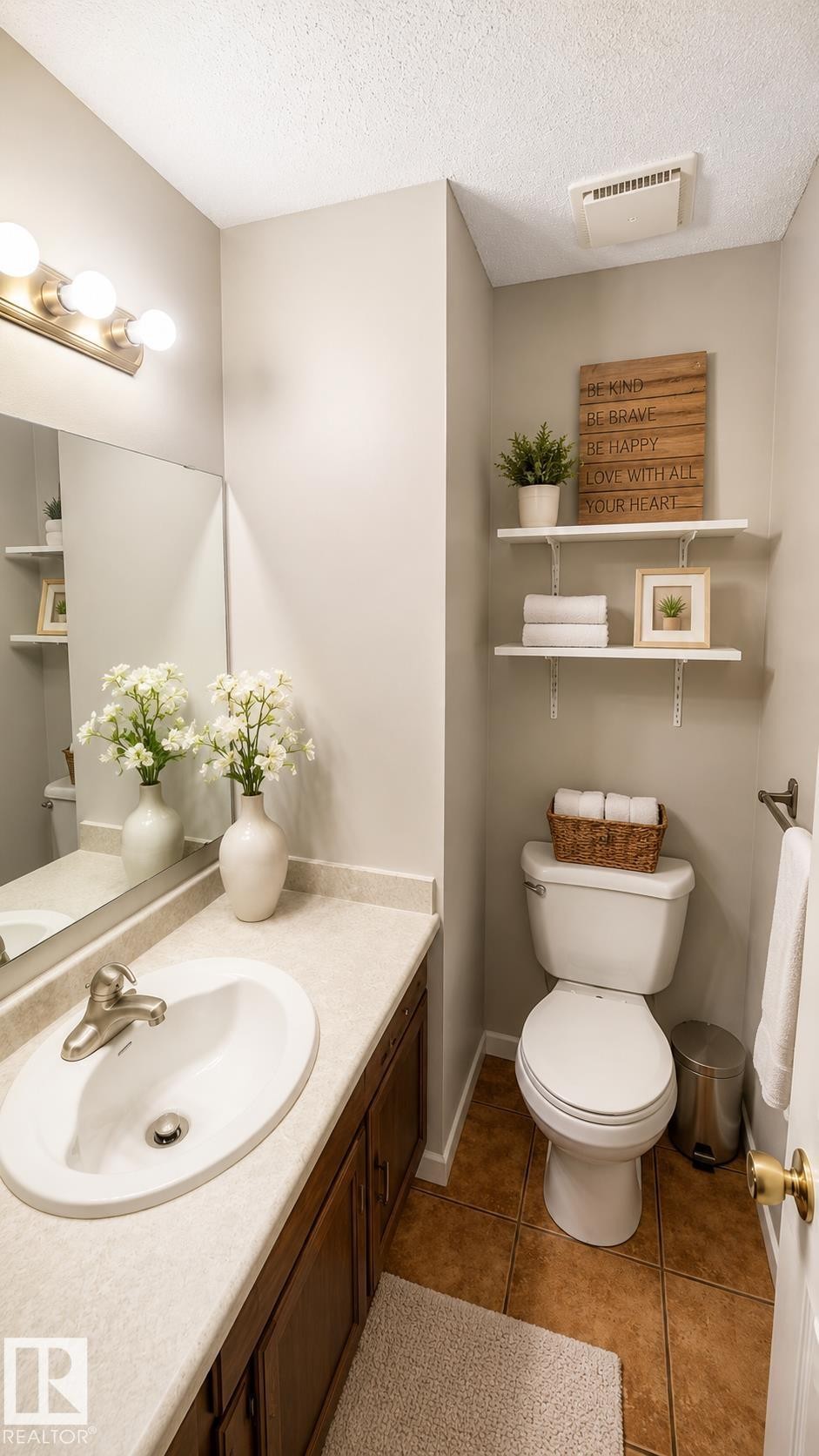 Bathroom featuring a vanity with dark wood-finish cabinetry and a light-toned countertop, a rectangular mirror, a three-light fixture with brushed nickel accents, and warm-toned floor tiles - 1022 106 Street Nw, Edmonton, AB - Indoor Photo Showing Bathroom