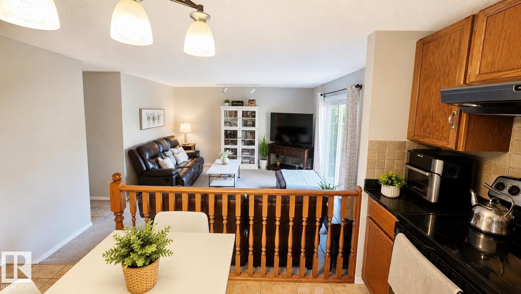 Kitchen with wood cabinetry, black countertops, and a tiled backsplash, offering a partial view into the living area featuring a sliding glass door - 1022 106 Street Nw, Edmonton, AB - Indoor