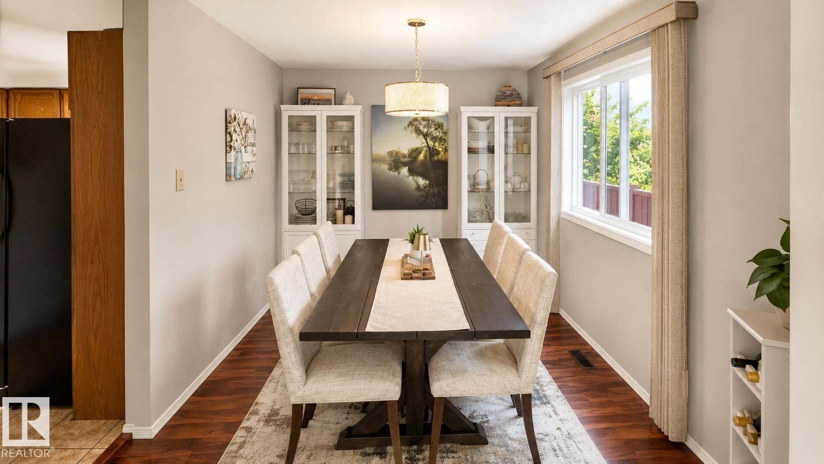 Dining area featuring wood-finish flooring, a contemporary chandelier, two built-in display cabinets, and a white-framed window with exterior green foliage - 1022 106 Street Nw, Edmonton, AB - Indoor Photo Showing Dining Room
