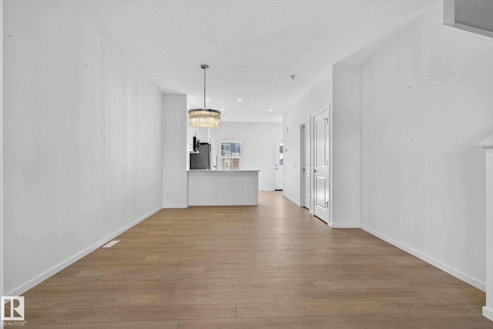 Open-concept living area featuring wood-finish flooring, white walls, and a contemporary chandelier - 264 Orchards Boulevard Sw, Edmonton, AB - Indoor