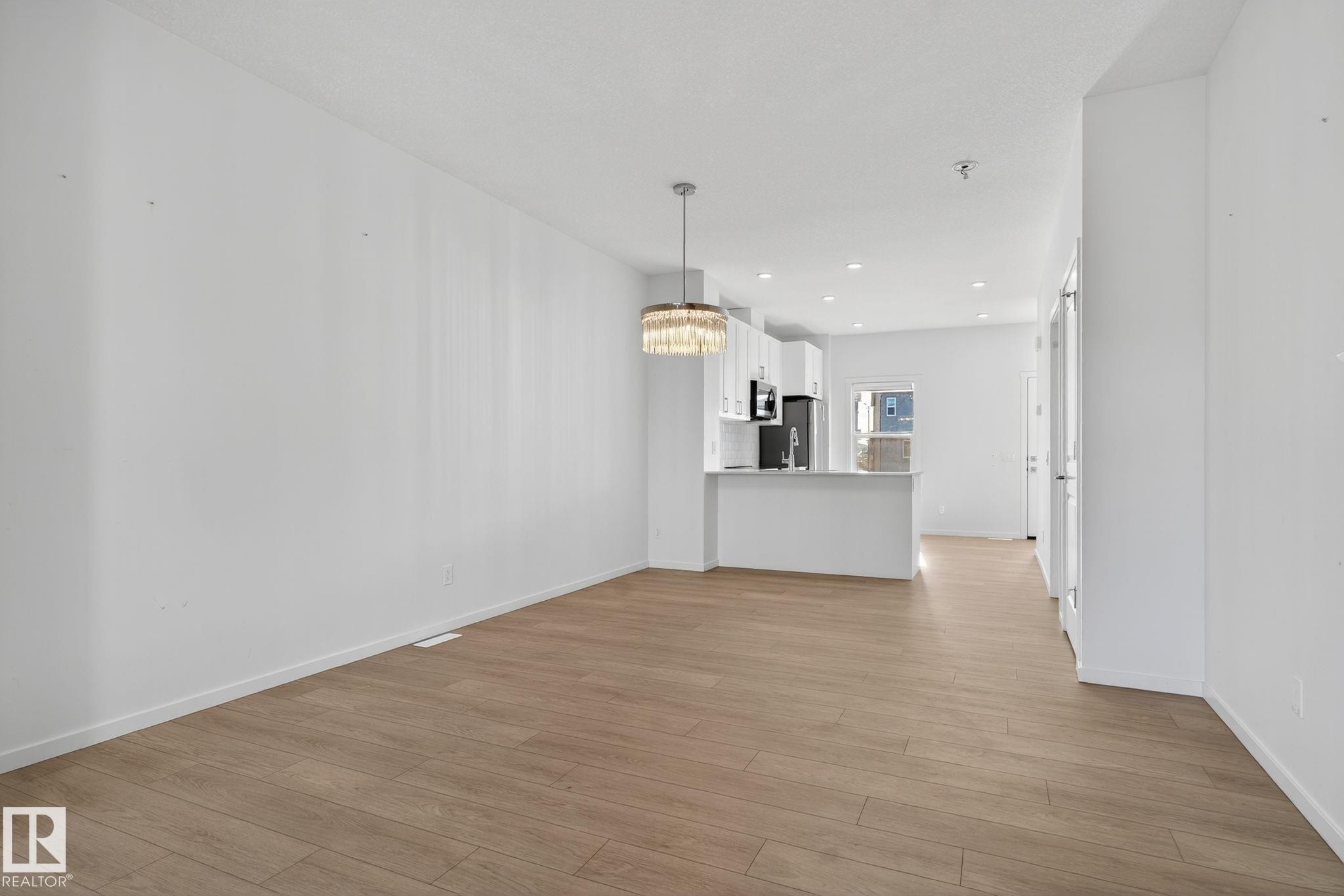 Open-concept living space featuring wood-finish flooring, recessed lighting, and a contemporary chandelier - 264 Orchards Boulevard Sw, Edmonton, AB - Indoor