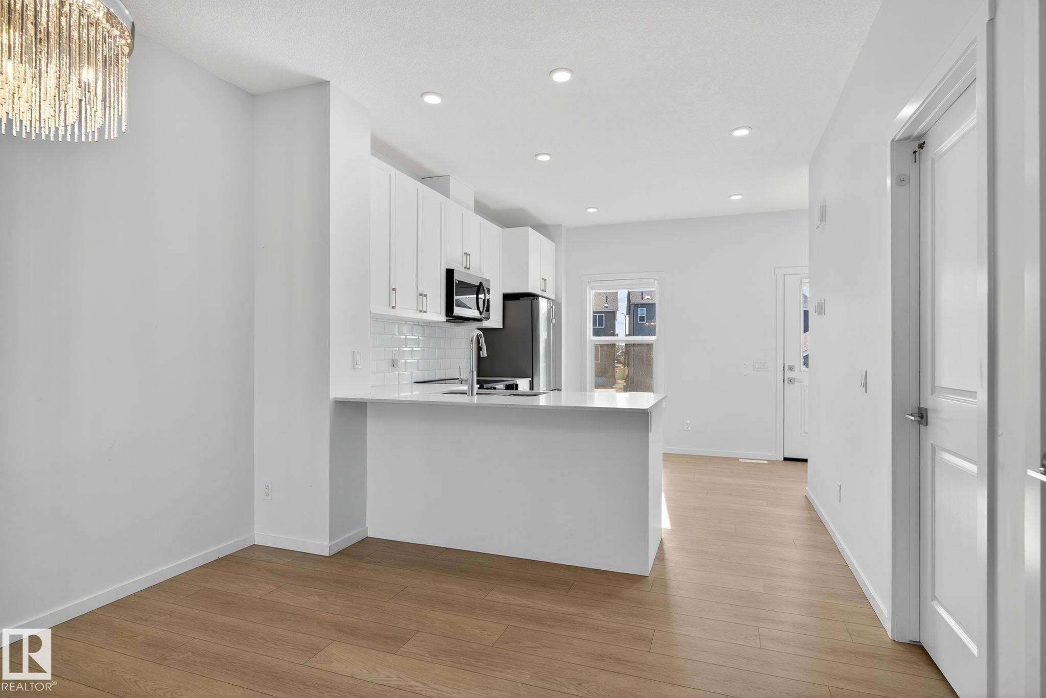 Open-concept kitchen and dining area featuring light wood-finish flooring, white cabinetry, integrated stainless steel appliances, a white subway tile backsplash, and a contemporary crystal-style chandelier - 264 Orchards Boulevard Sw, Edmonton, AB - Indoor Photo Showing Kitchen