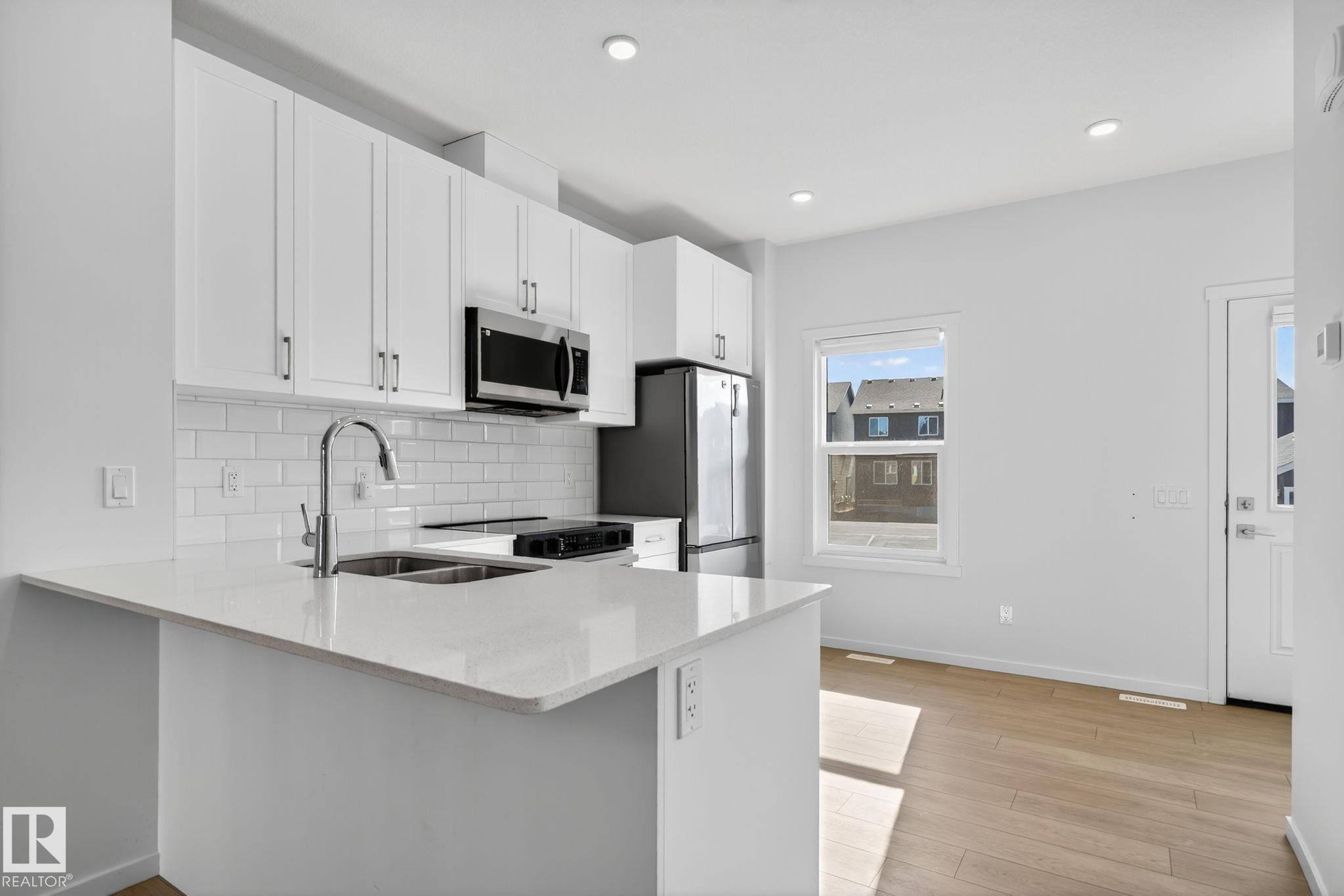 Modern kitchen featuring white shaker cabinetry, stainless steel appliances, a subway tile backsplash, and light wood-finish flooring - 264 Orchards Boulevard Sw, Edmonton, AB - Indoor Photo Showing Kitchen With Double Sink With Upgraded Kitchen