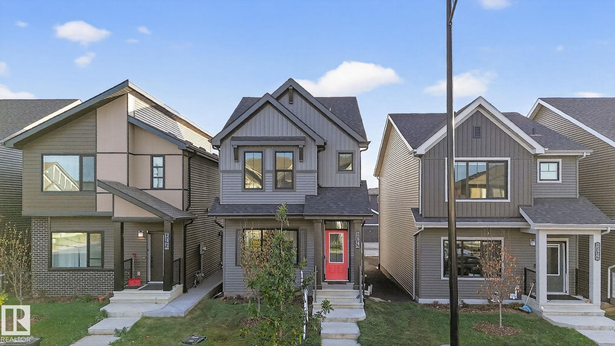 Contemporary gray siding residence featuring a bold red entry door, a covered front porch, and black-framed windows - 264 Orchards Boulevard Sw, Edmonton, AB - Outdoor With Facade