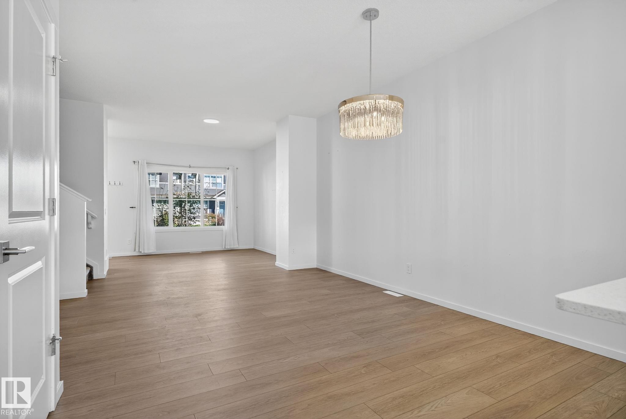 Spacious interior featuring wood-finish flooring, a contemporary chandelier, large picture windows, and white painted trim - 264 Orchards Boulevard Sw, Edmonton, AB - Indoor
