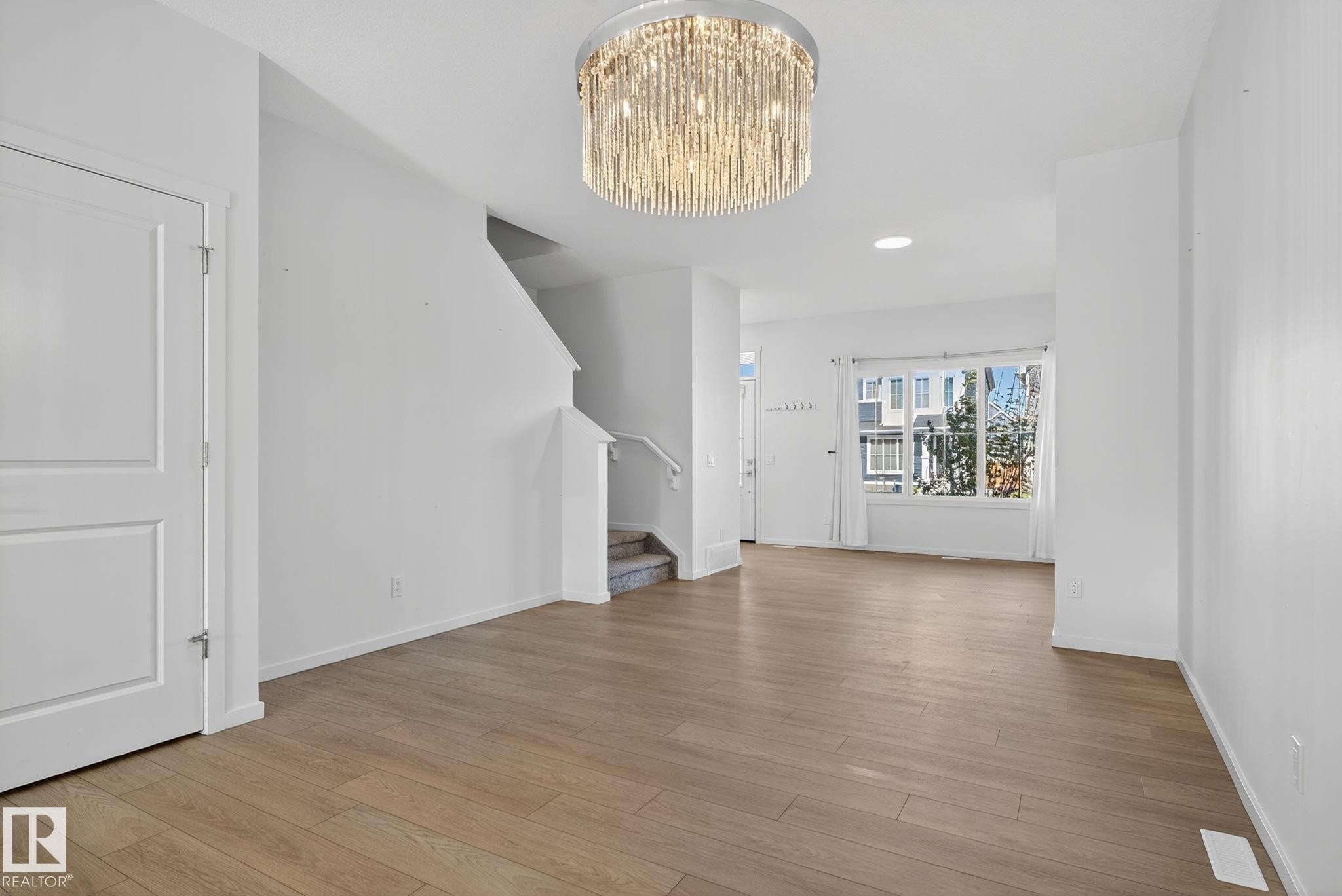 Open living area featuring wood-finish flooring, a contemporary crystal chandelier, and bright white walls - 264 Orchards Boulevard Sw, Edmonton, AB - Indoor Photo Showing Other Room