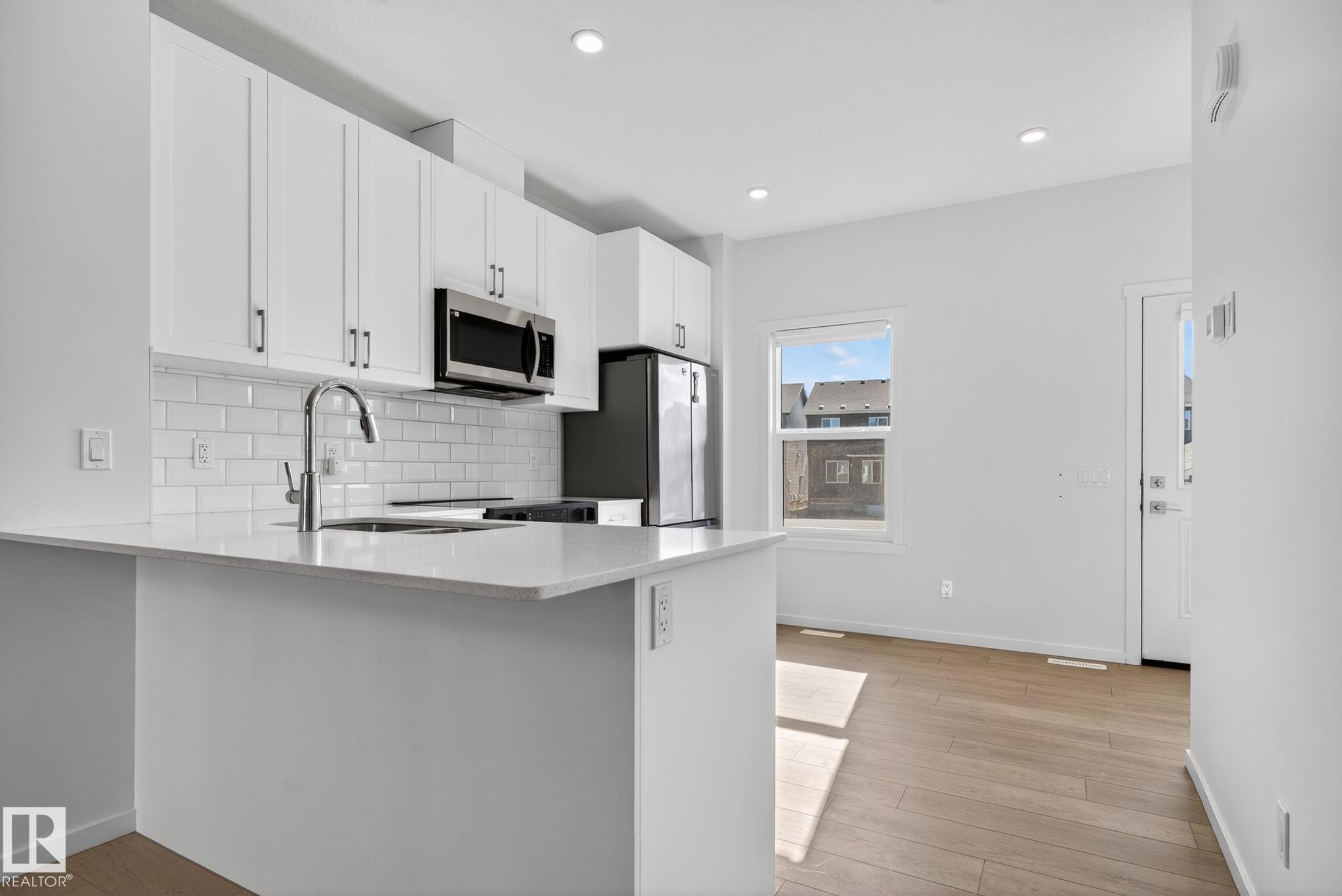 Contemporary kitchen featuring white cabinetry, stainless steel appliances, a subway tile backsplash, and light wood-finish flooring - 264 Orchards Boulevard Sw, Edmonton, AB - Indoor Photo Showing Kitchen With Upgraded Kitchen