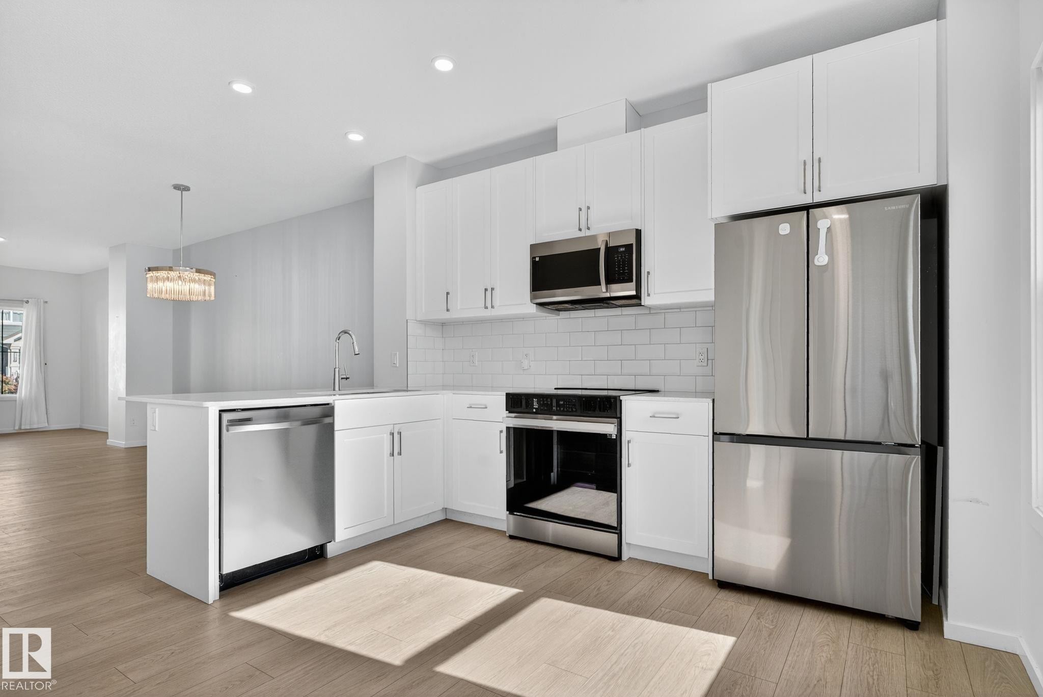 Modern kitchen featuring white cabinetry, stainless steel appliances, and wood-finish flooring - 264 Orchards Boulevard Sw, Edmonton, AB - Indoor Photo Showing Kitchen