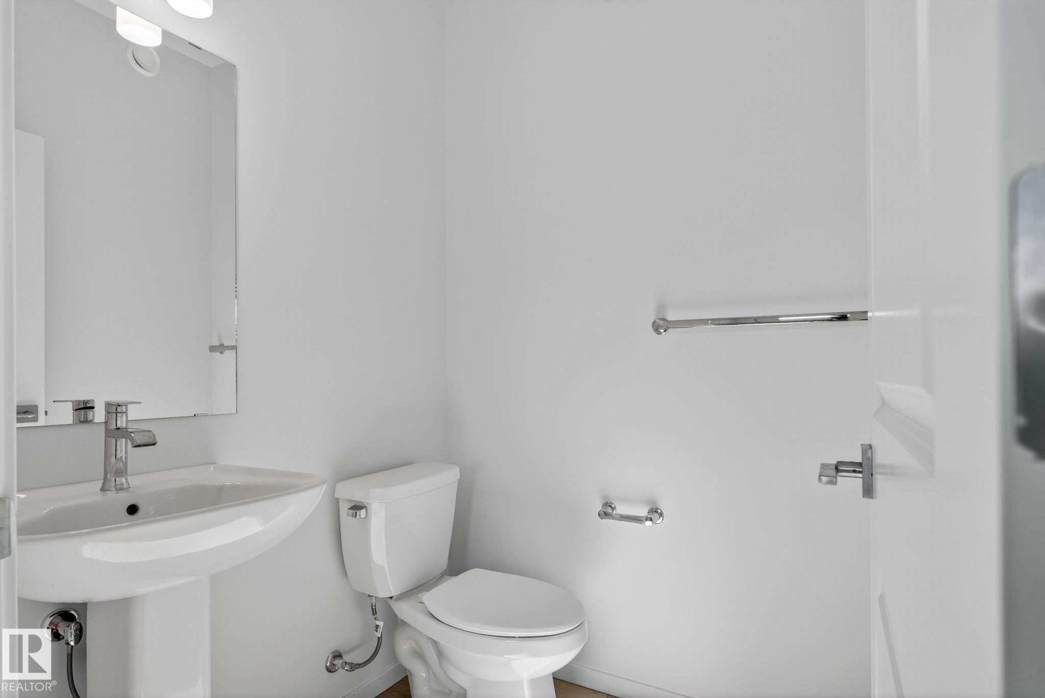 Powder room featuring a pedestal sink with chrome fixtures, a wall-mounted rectangular mirror, and a contemporary vanity light - 264 Orchards Boulevard Sw, Edmonton, AB - Indoor Photo Showing Bathroom