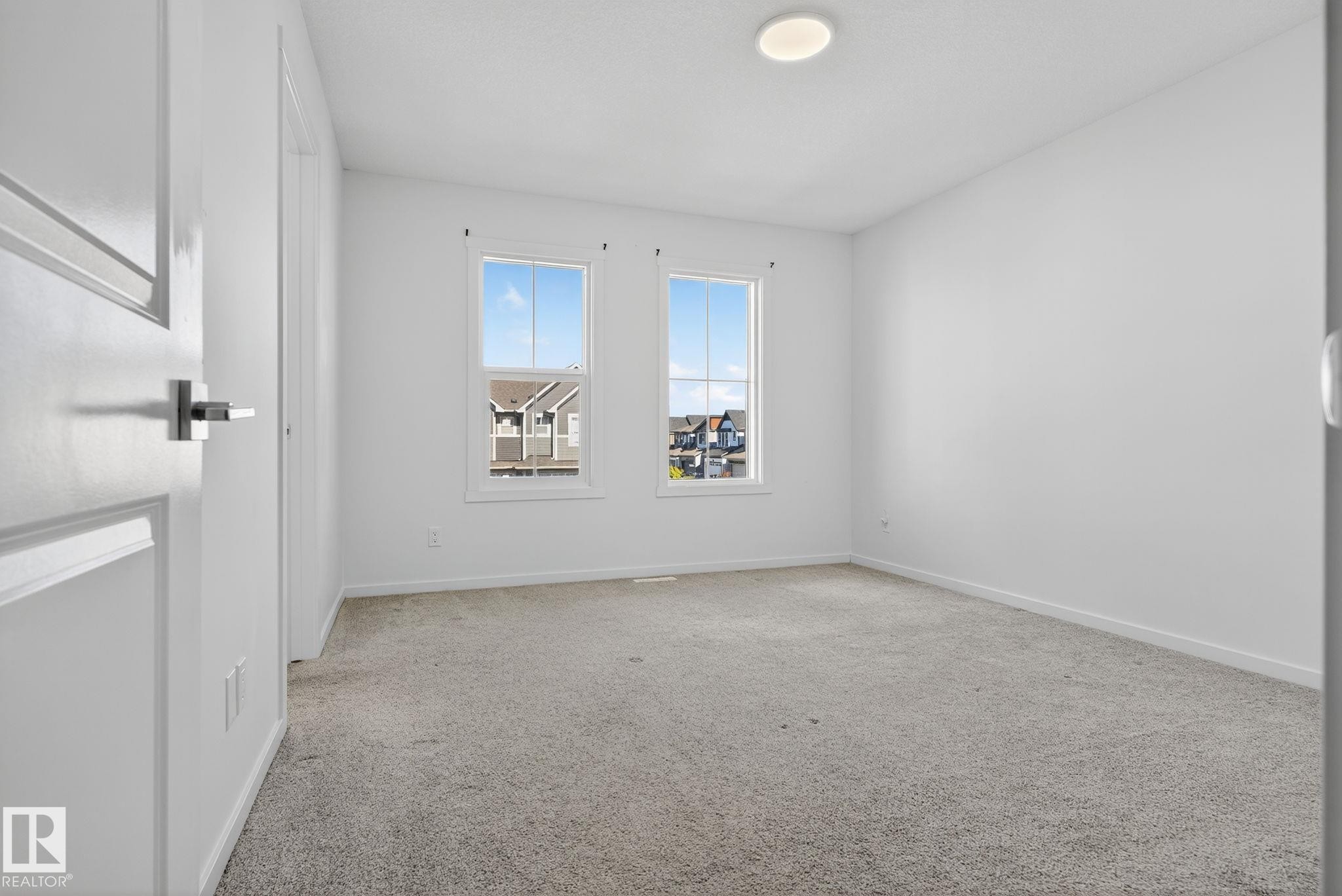 Bright interior room featuring a light-colored carpet, two double-hung windows, a flush-mount ceiling light fixture, and white trim - 264 Orchards Boulevard Sw, Edmonton, AB - Indoor Photo Showing Other Room