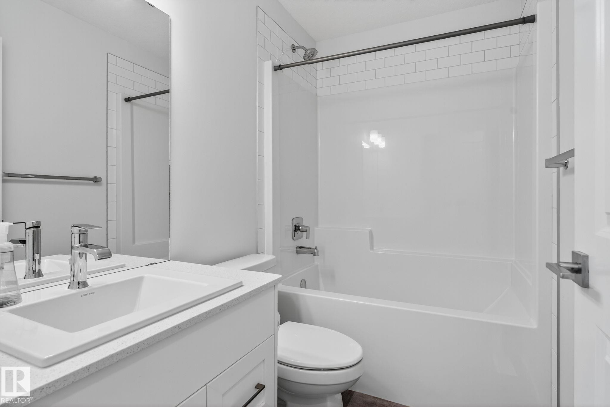 Bathroom featuring a white bathtub with subway tile surround, chrome fixtures, a modern vanity with integrated sink, and a large wall-mounted mirror - 264 Orchards Boulevard Sw, Edmonton, AB - Indoor Photo Showing Bathroom