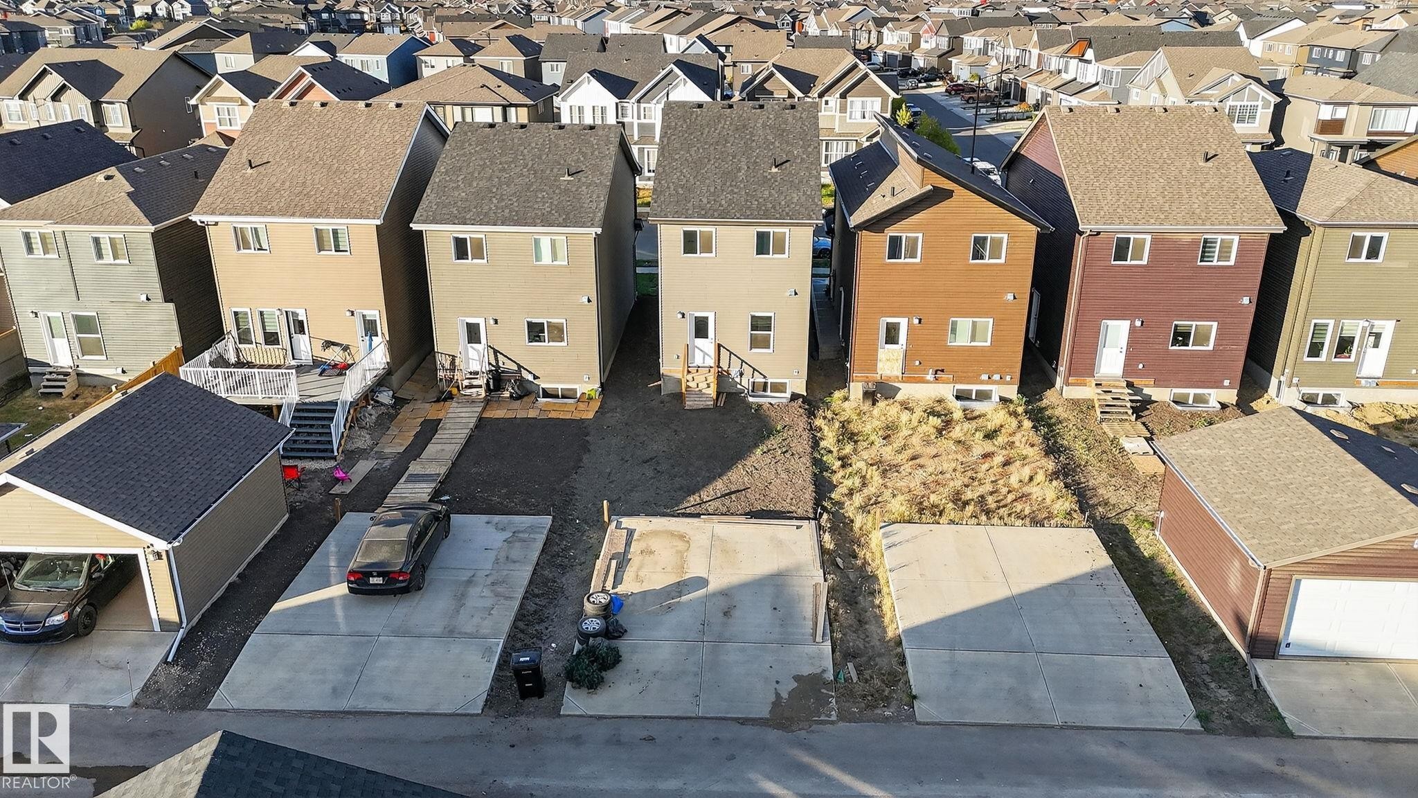 Rear exterior featuring light-colored siding, a white deck with stairs, a concrete patio, and a detached garage with a dark shingle roof - 264 Orchards Boulevard Sw, Edmonton, AB - Outdoor