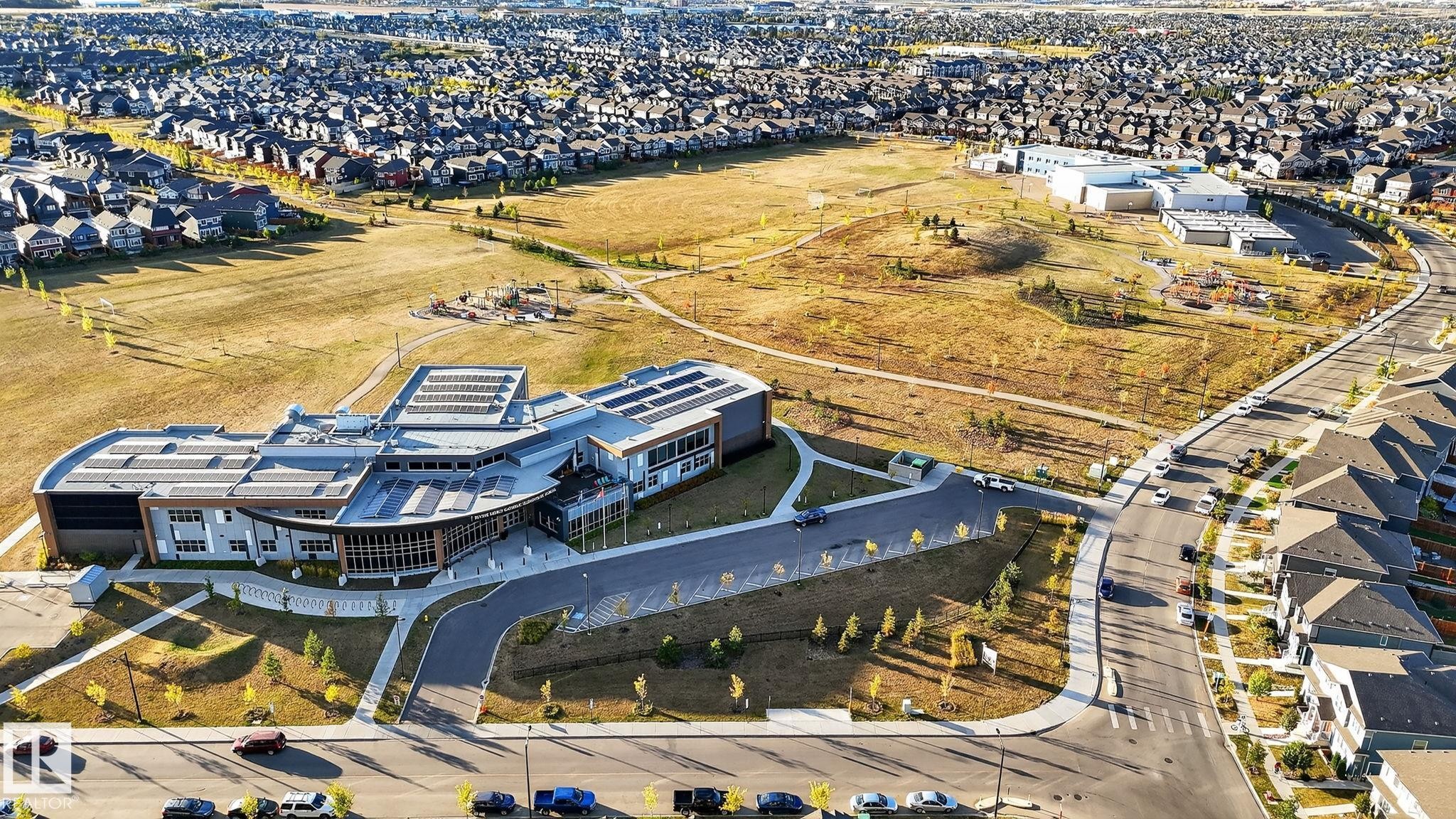 Expansive community featuring modern residential properties and a contemporary educational facility with solar panel installations - 264 Orchards Boulevard Sw, Edmonton, AB - Outdoor With View