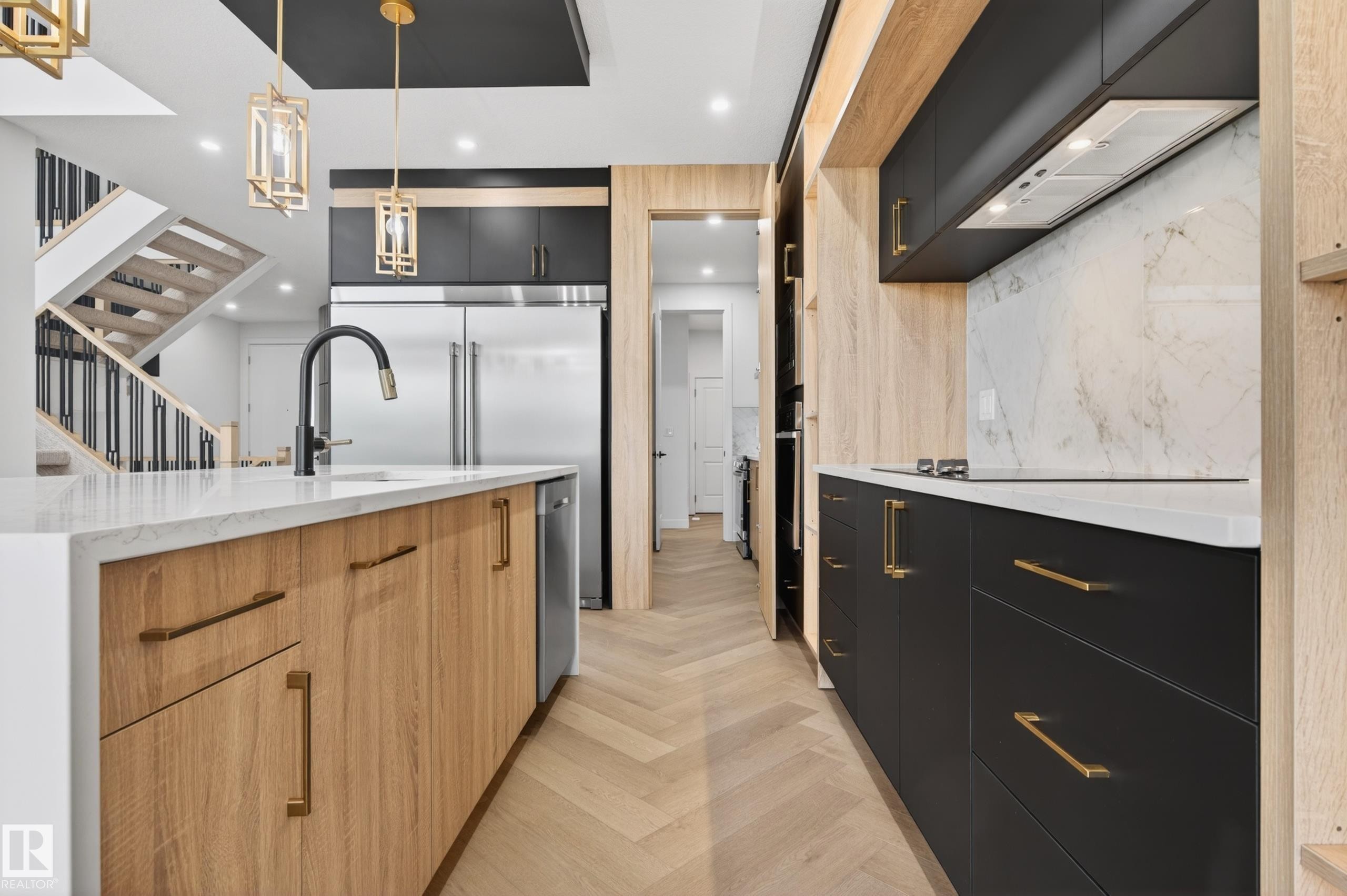 Contemporary kitchen featuring a large waterfall island with integrated sink and matte black faucet, herringbone wood-finish flooring, and two-tone cabinetry with gold-tone hardware - 431 172 Avenue, Edmonton, AB - Indoor Photo Showing Kitchen