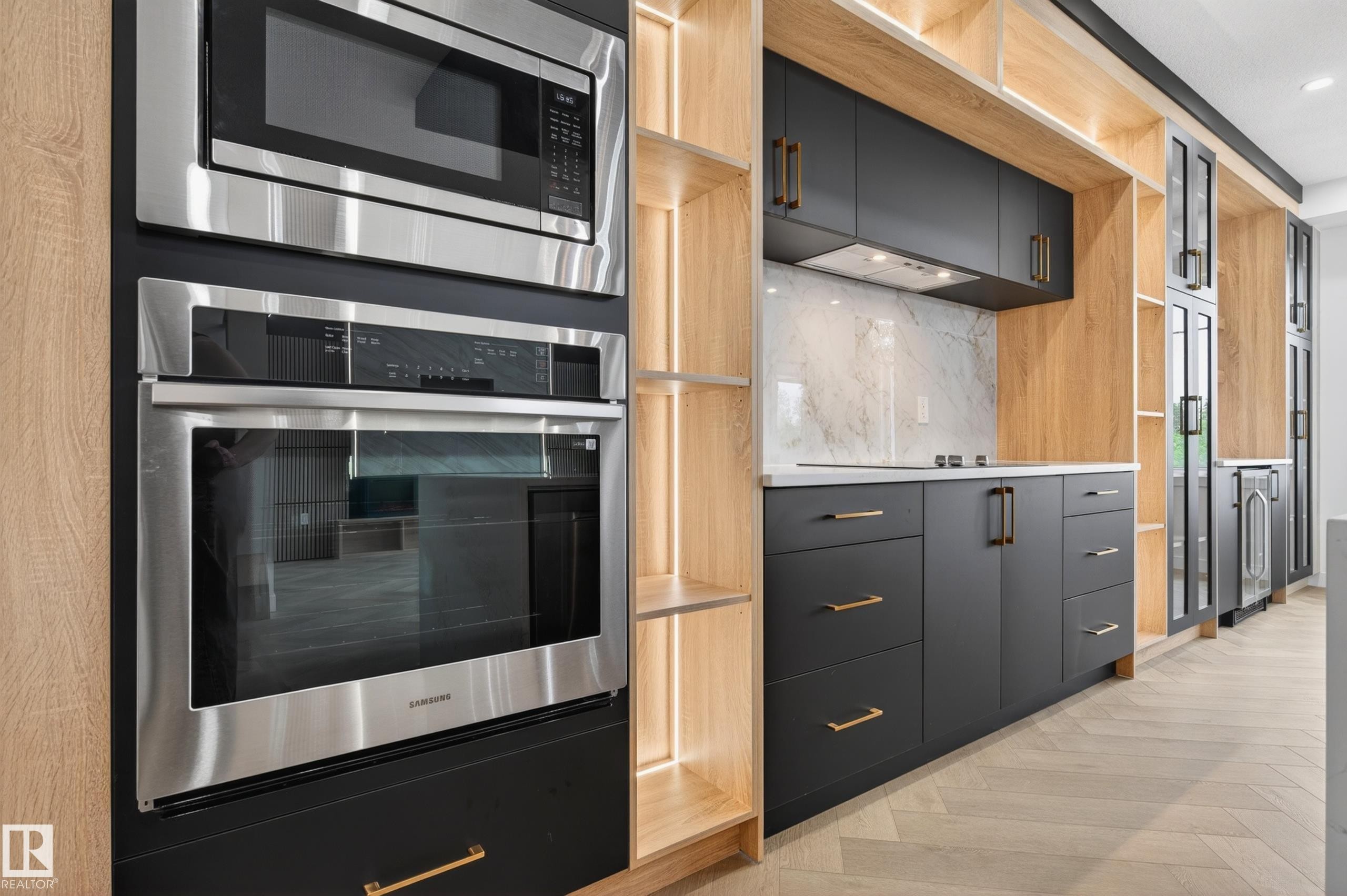 Modern kitchen featuring integrated stainless steel appliances, contrasting dark cabinetry with brass hardware, light wood-finish open shelving, a white marble-patterned backsplash, and light-toned wood-finish flooring - 431 172 Avenue, Edmonton, AB - Indoor Photo Showing Kitchen