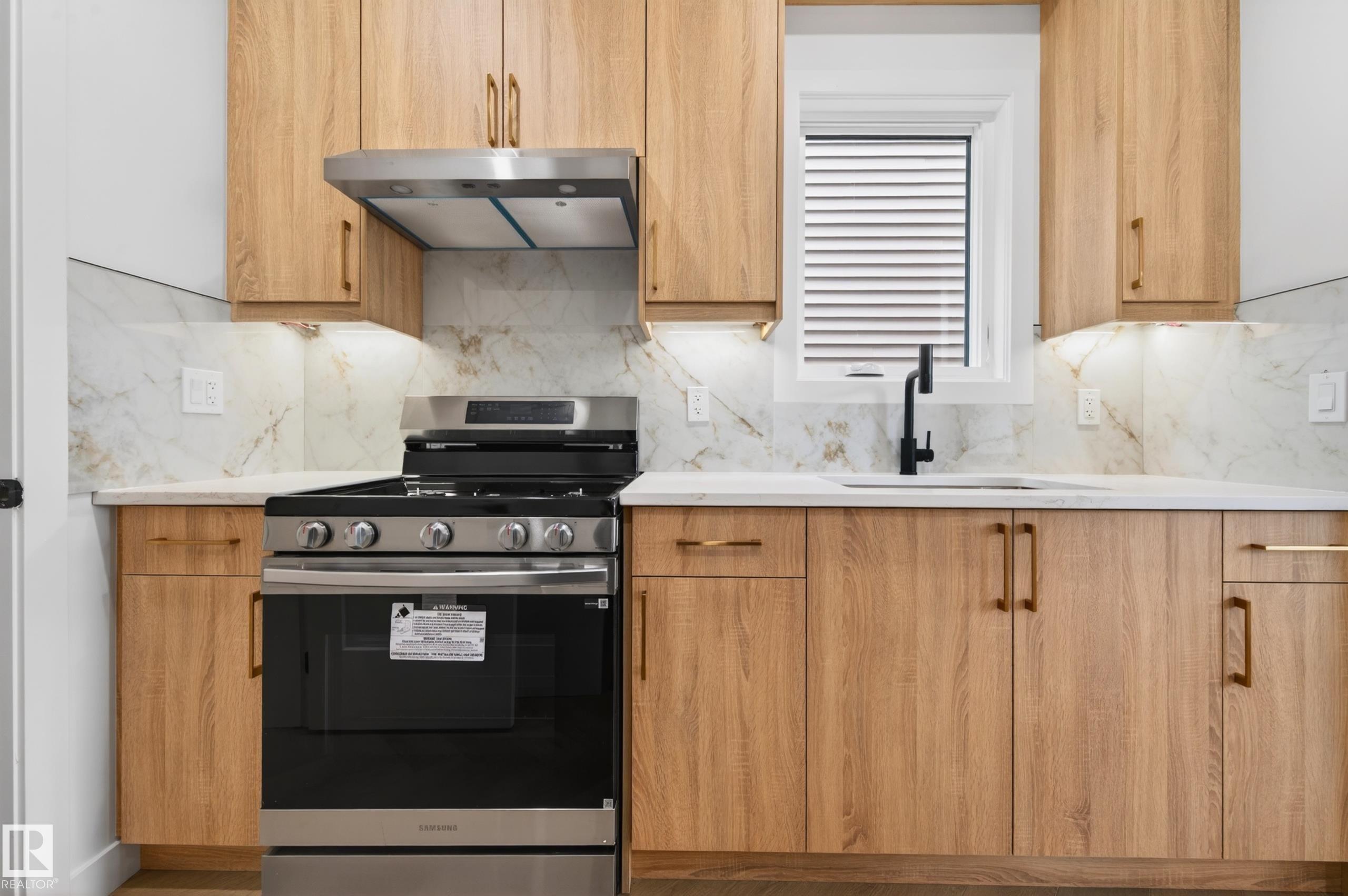 Kitchen featuring wood-finish cabinetry with gold-tone hardware, white countertops, and a marble-patterned backsplash - 431 172 Avenue, Edmonton, AB - Indoor Photo Showing Kitchen