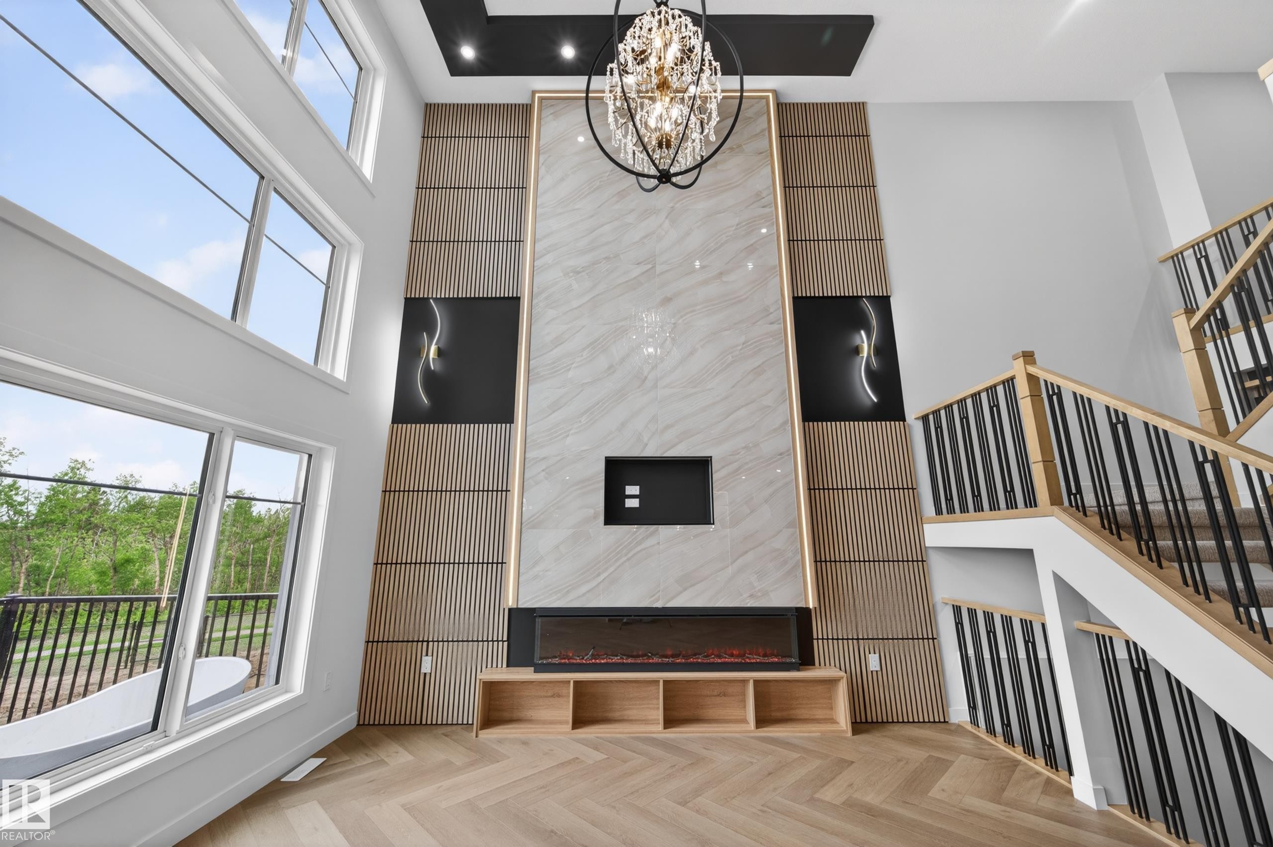 Double-height living space featuring an electric fireplace with a floor-to-ceiling stone-look surround, integrated shelving, and a decorative chandelier - 431 172 Avenue, Edmonton, AB - Indoor Photo Showing Other Room