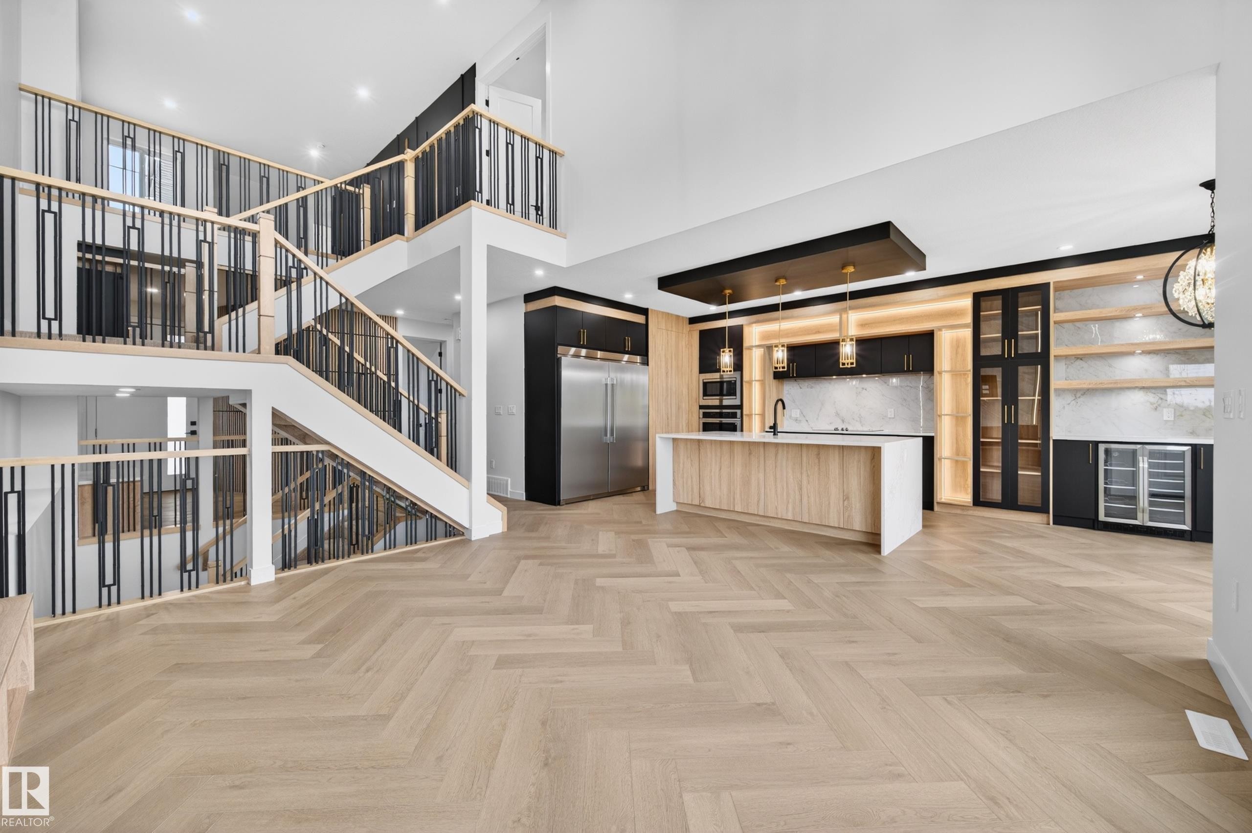 Open-concept living space featuring herringbone wood-finish flooring, a contemporary kitchen with a large island and integrated appliances, and a multi-level staircase with modern black and wood railings - 431 172 Avenue, Edmonton, AB - Indoor