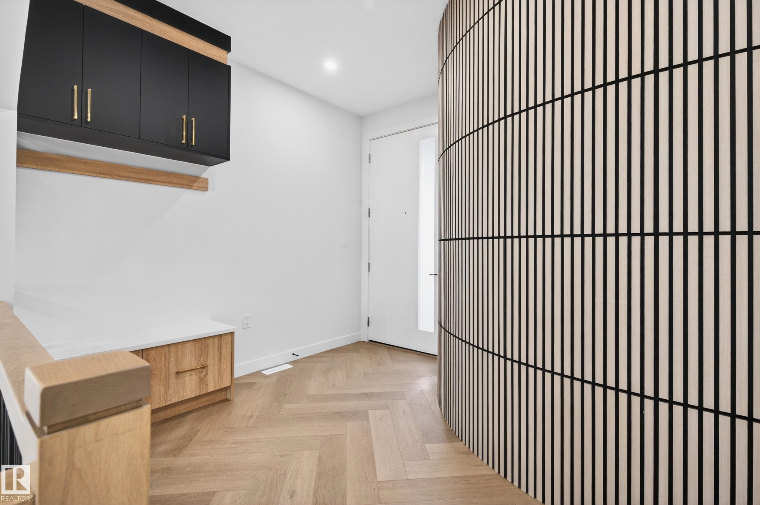 Entryway featuring a curved slatted wood wall, herringbone-patterned wood-finish flooring, built-in black cabinetry with gold hardware, a white built-in bench with wood-finish drawers, and a wood-finish stair railing - 431 172 Avenue, Edmonton, AB - Indoor Photo Showing Other Room