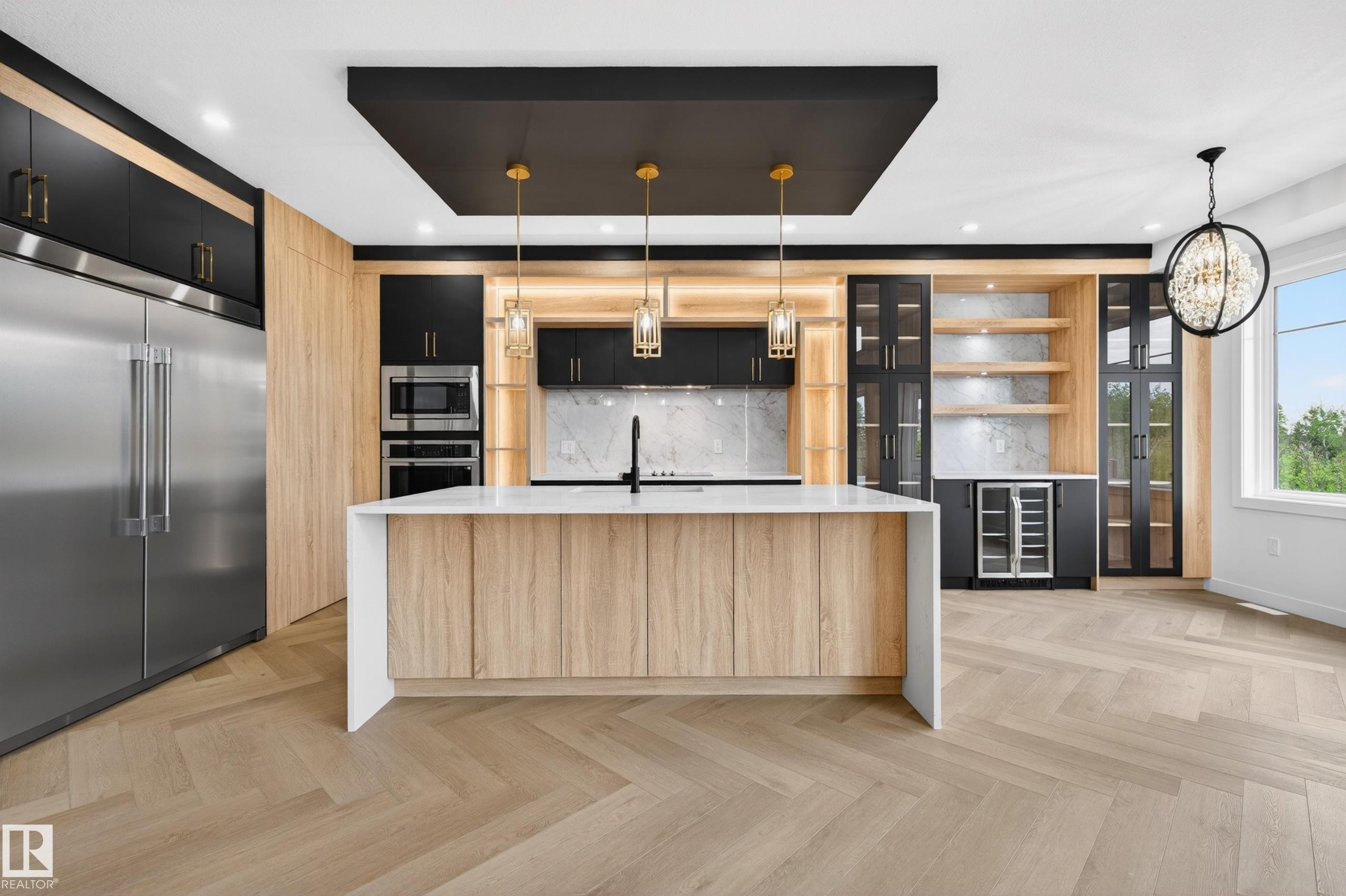 Chef's kitchen featuring a large central island with a waterfall countertop, herringbone wood-finish flooring, integrated stainless steel appliances, black cabinetry with gold-tone hardware, and a built-in beverage refrigerator - 431 172 Avenue, Edmonton, AB - Indoor Photo Showing Kitchen