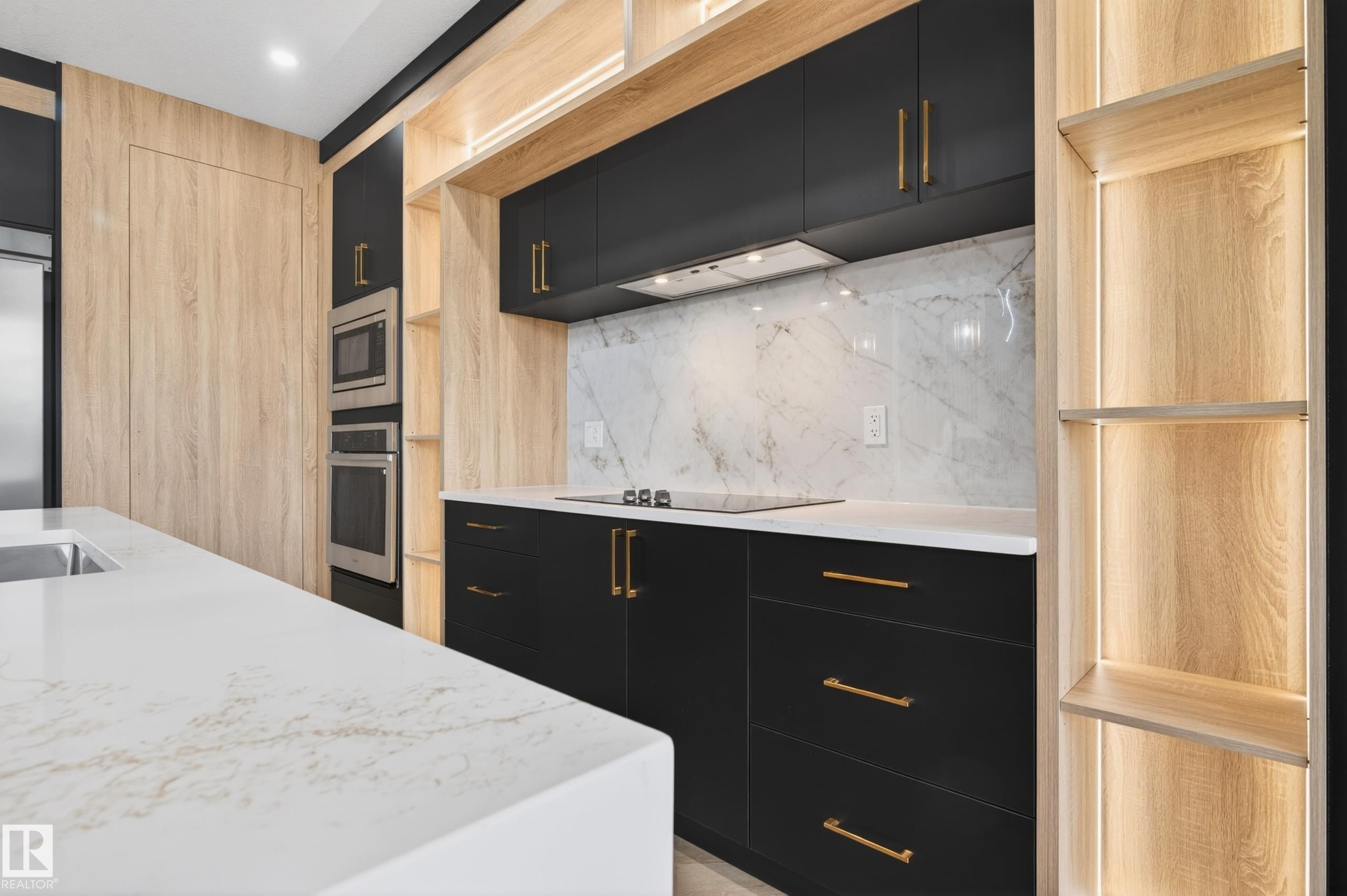 Modern kitchen featuring dark cabinetry with gold hardware, integrated stainless steel appliances, a white quartz island with an undermount sink, a white marble backsplash, and wood-finish shelving with integrated lighting - 431 172 Avenue, Edmonton, AB - Indoor Photo Showing Kitchen With Upgraded Kitchen