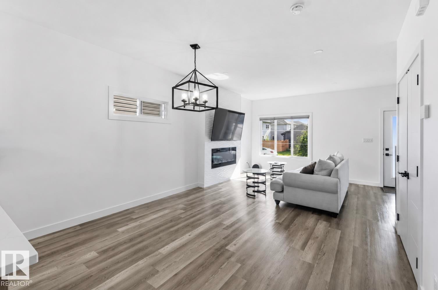 Spacious living area featuring wood-finish flooring, a contemporary fireplace with white tile surround, and a large window providing outdoor illumination - 17924 61 Street Nw, Edmonton, AB - Indoor Photo Showing Living Room With Fireplace