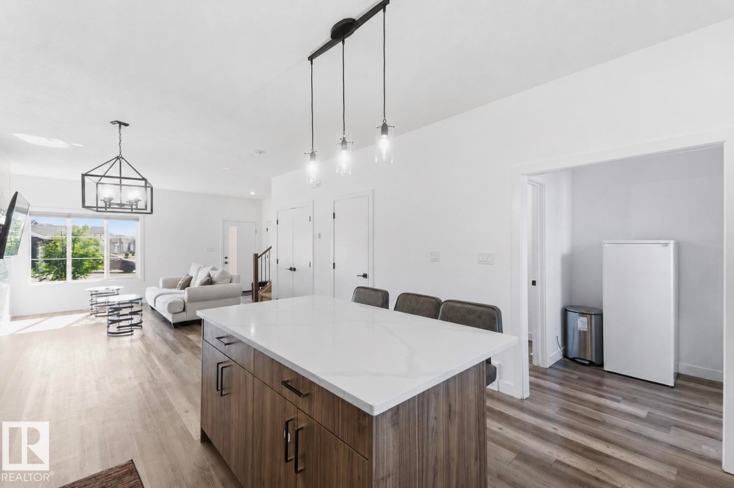 Spacious kitchen island with a light-toned countertop, wood-finish cabinetry, and seating for three - 17924 61 Street Nw, Edmonton, AB - Indoor