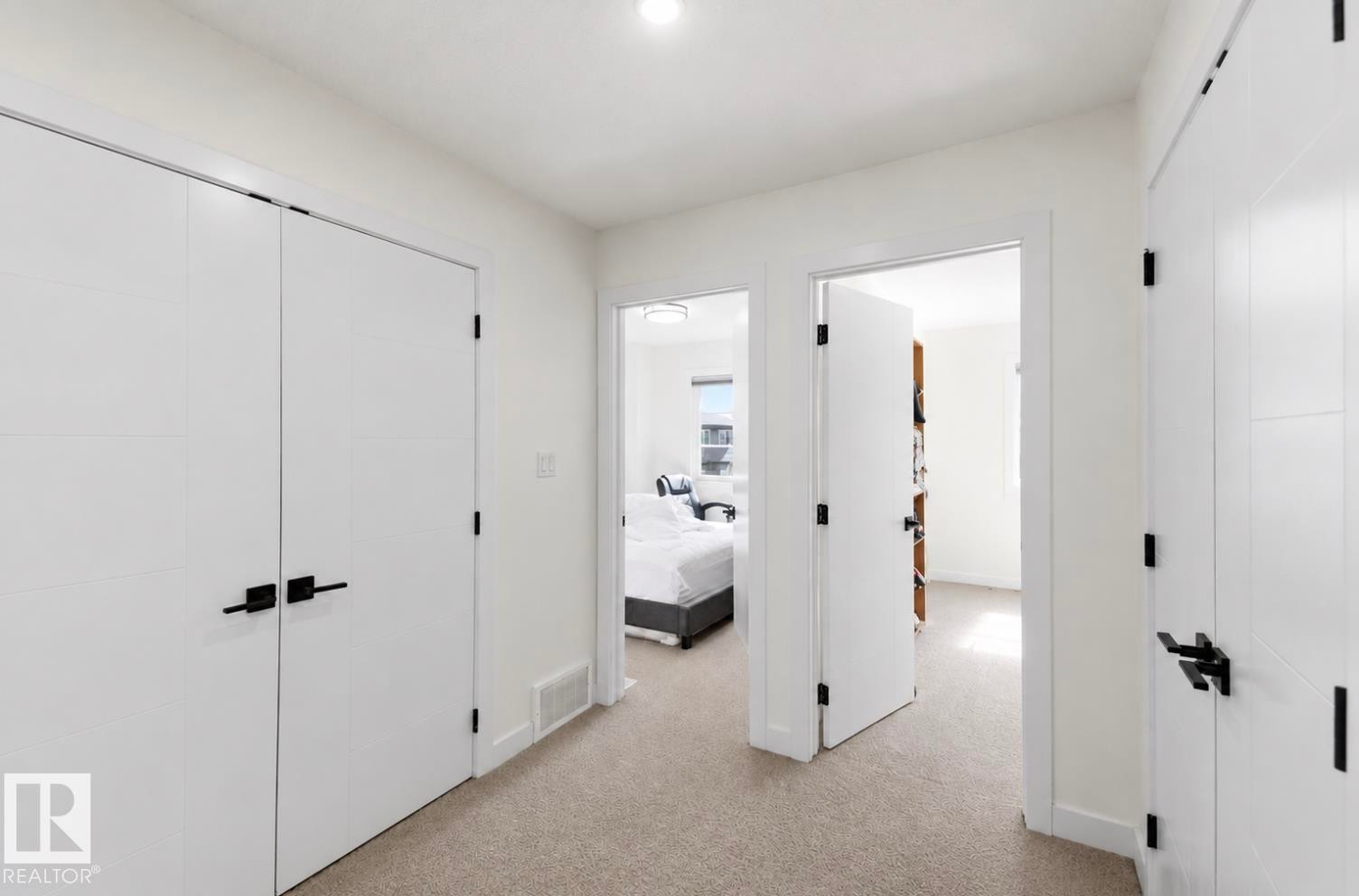 Hallway featuring light-toned carpeting, white walls, and modern white doors with black hardware - 17924 61 Street Nw, Edmonton, AB - Indoor Photo Showing Other Room