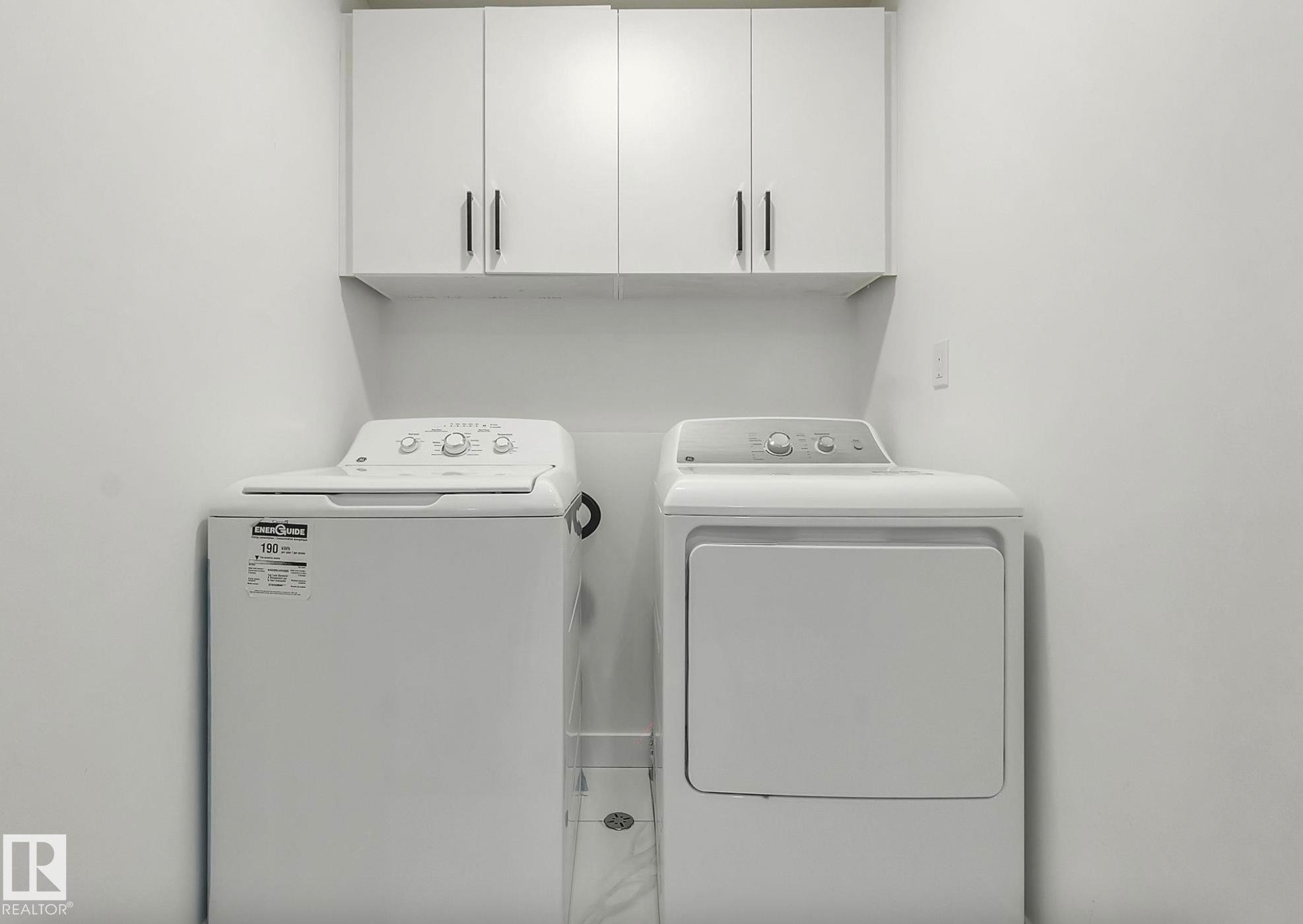 Dedicated laundry area featuring white wall-mounted cabinetry with dark pulls, a white top-load washing machine, and a white front-load dryer - 17924 61 Street Nw, Edmonton, AB - Indoor Photo Showing Laundry Room