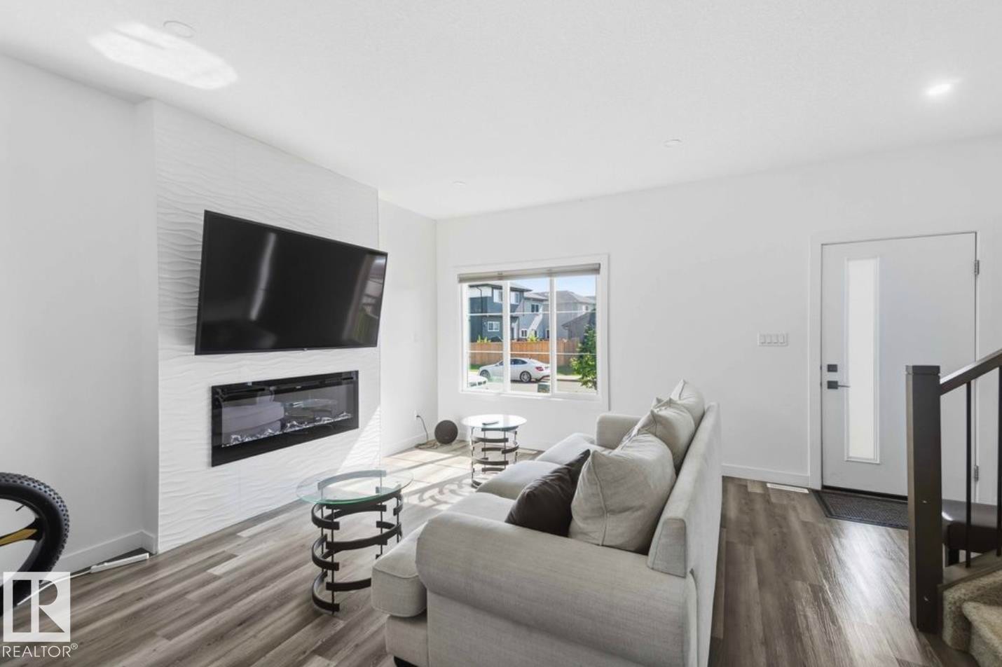 Living area featuring a textured accent wall with a built-in electric fireplace, wood-finish flooring, and a contemporary entry door with a frosted glass insert - 17924 61 Street Nw, Edmonton, AB - Indoor Photo Showing Living Room With Fireplace