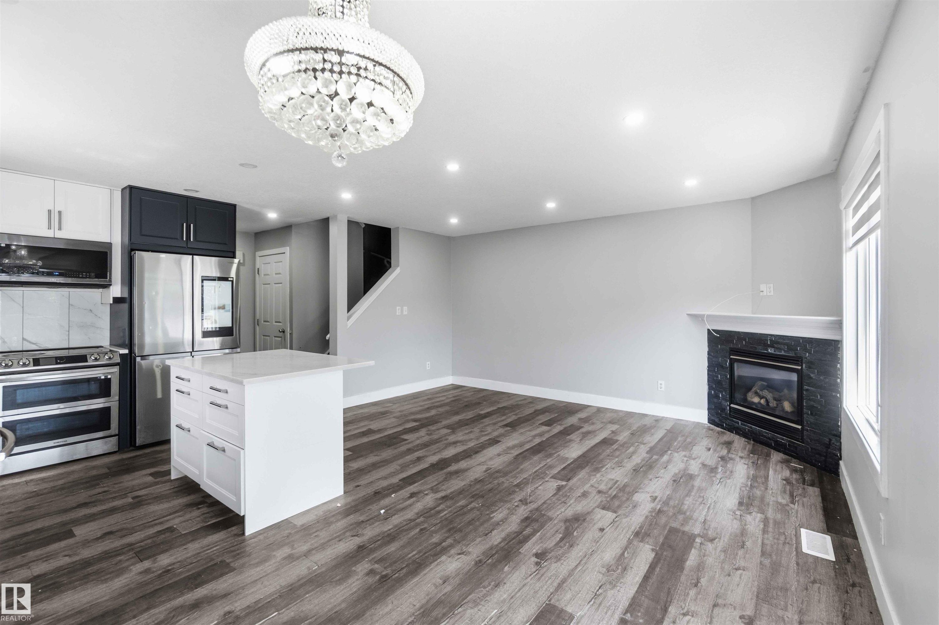 Open-concept living space with wood-finish flooring, a contemporary fireplace with a dark stone surround, and recessed lighting - #64 120 Magrath Rd Nw, Edmonton, AB - Indoor Photo Showing Kitchen With Fireplace
