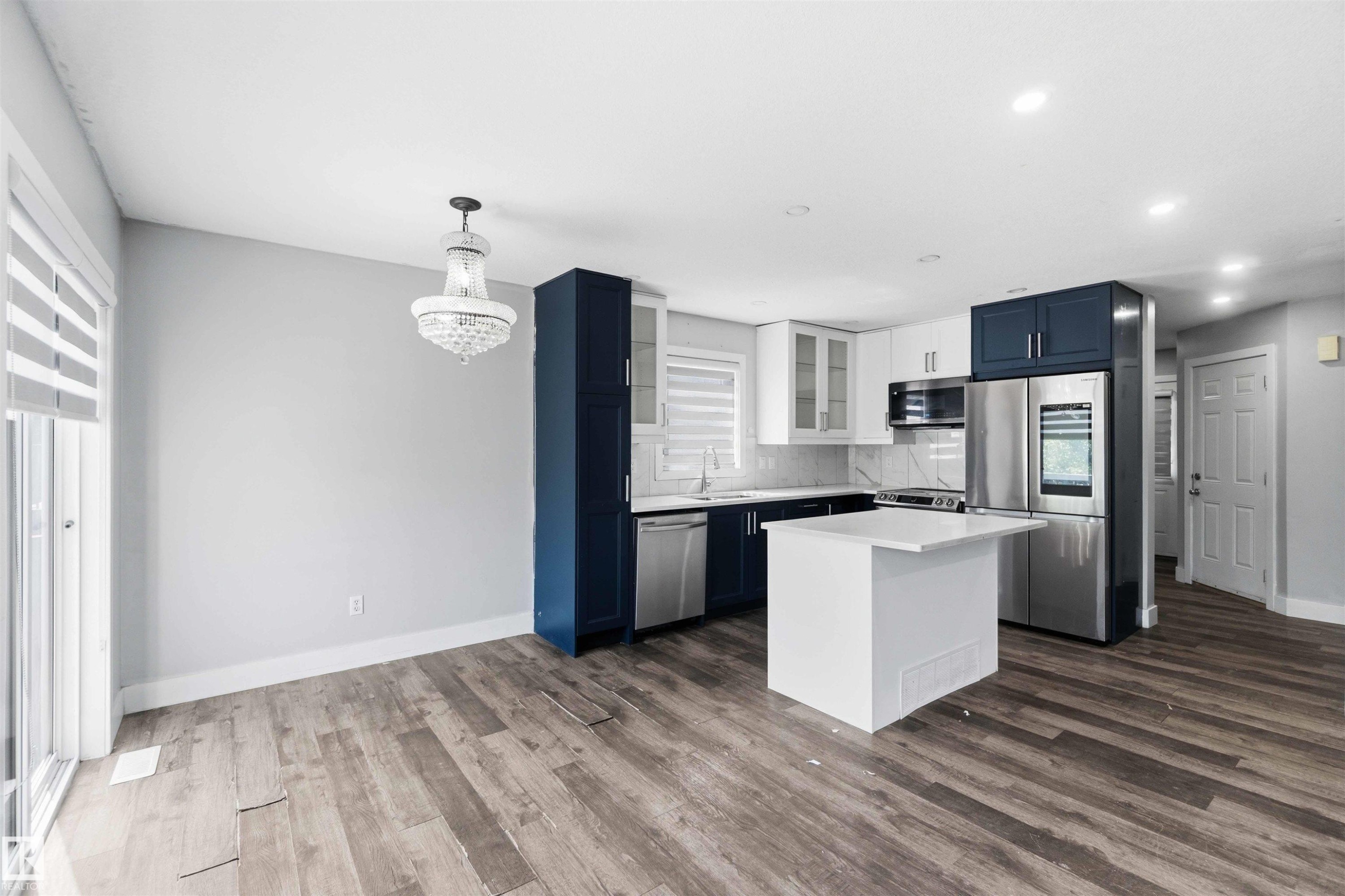 Modern kitchen featuring white and navy cabinetry, stainless steel appliances, a white island, and wood-finish flooring - #64 120 Magrath Rd Nw, Edmonton, AB - Indoor Photo Showing Kitchen