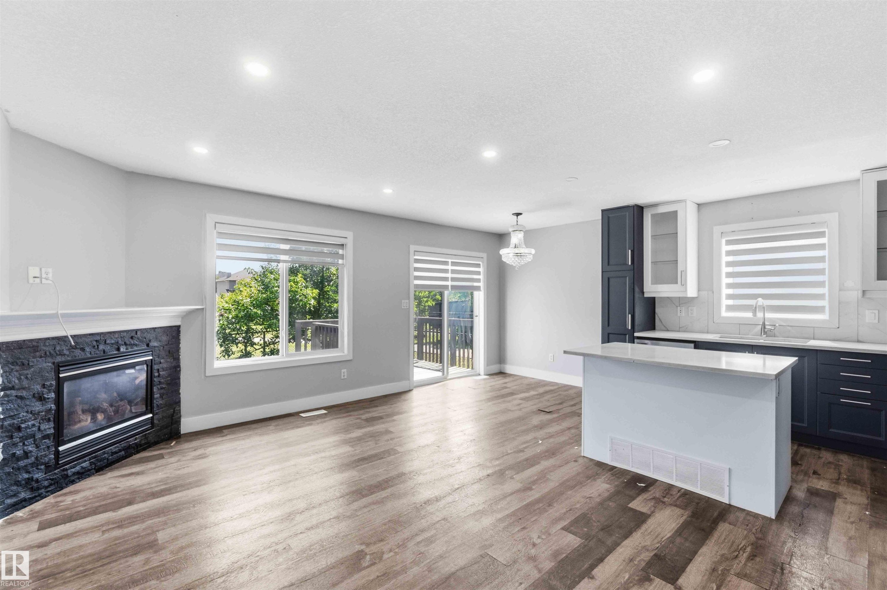 Open-concept living space with wood-finish flooring, a contemporary fireplace featuring black stacked stone, and recessed lighting - #64 120 Magrath Rd Nw, Edmonton, AB - Indoor With Fireplace