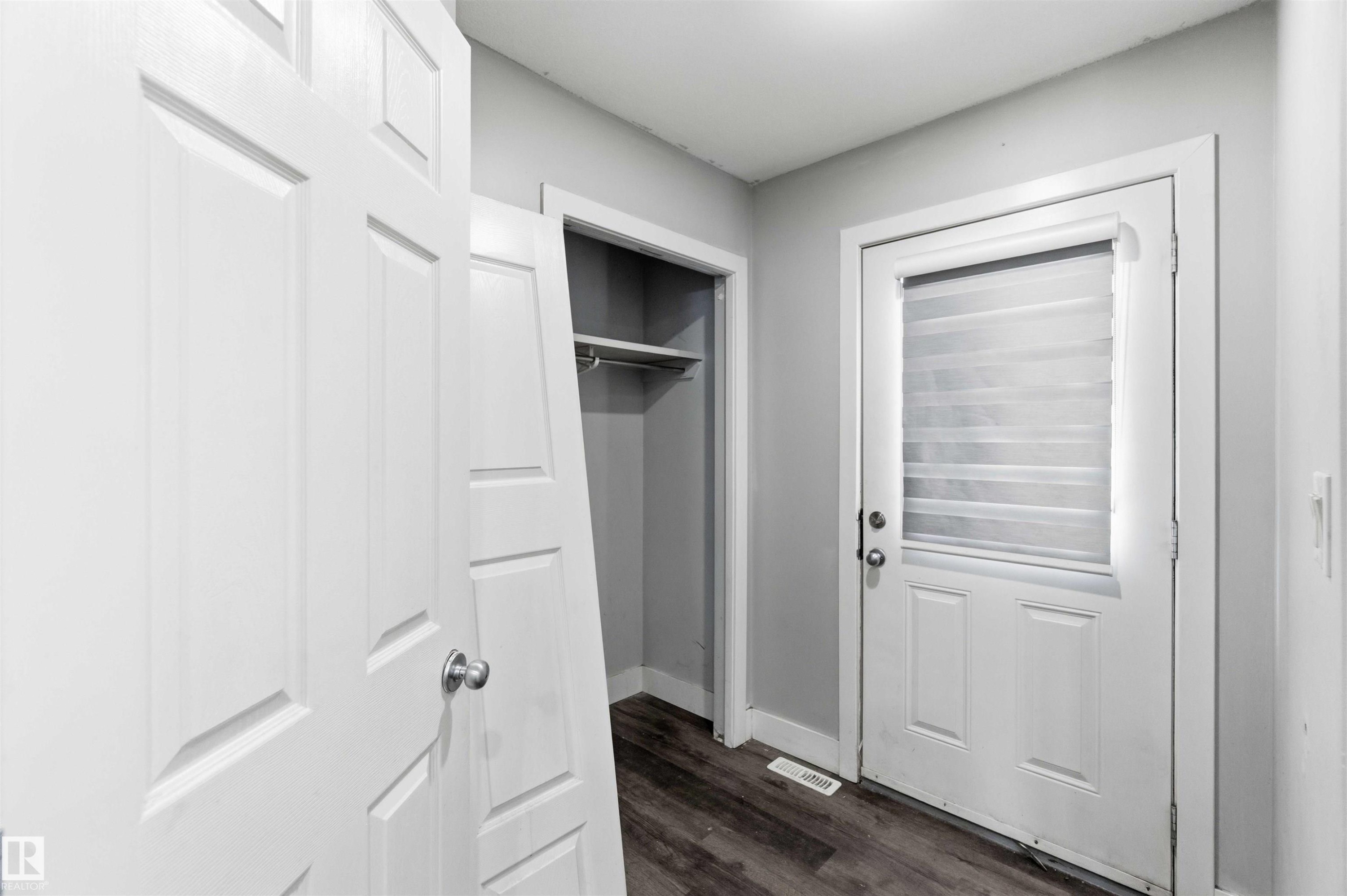 Entryway featuring a white paneled door with round silver hardware, a closet with shelving and a hanging rod, a white exterior door with an inset privacy blind, and wood-finish flooring - #64 120 Magrath Rd Nw, Edmonton, AB - Indoor Photo Showing Other Room