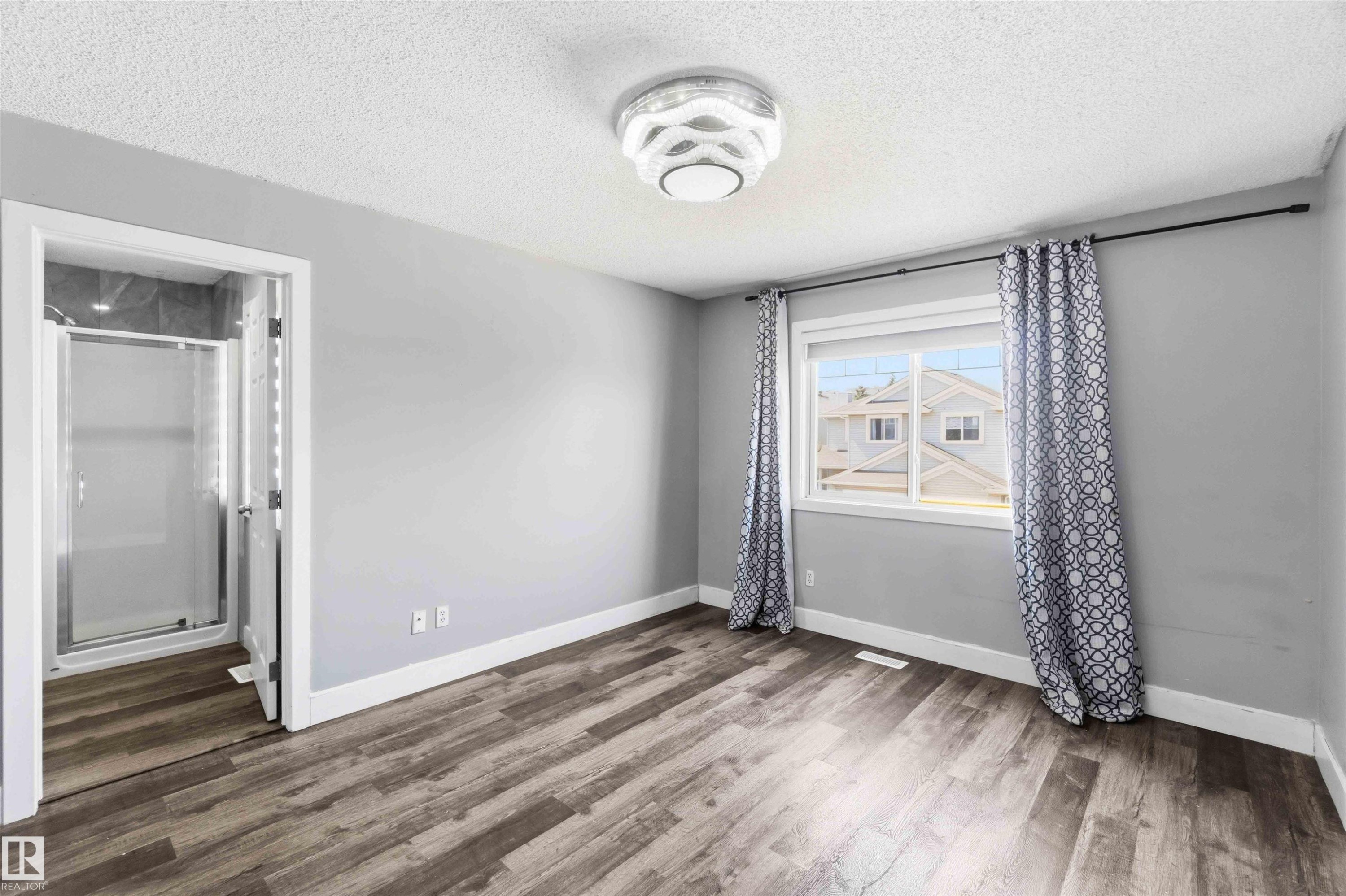 Light-filled room featuring wood-finish flooring, a contemporary ceiling light fixture, and a built-in shower enclosure with a glass door - #64 120 Magrath Rd Nw, Edmonton, AB - Indoor Photo Showing Other Room