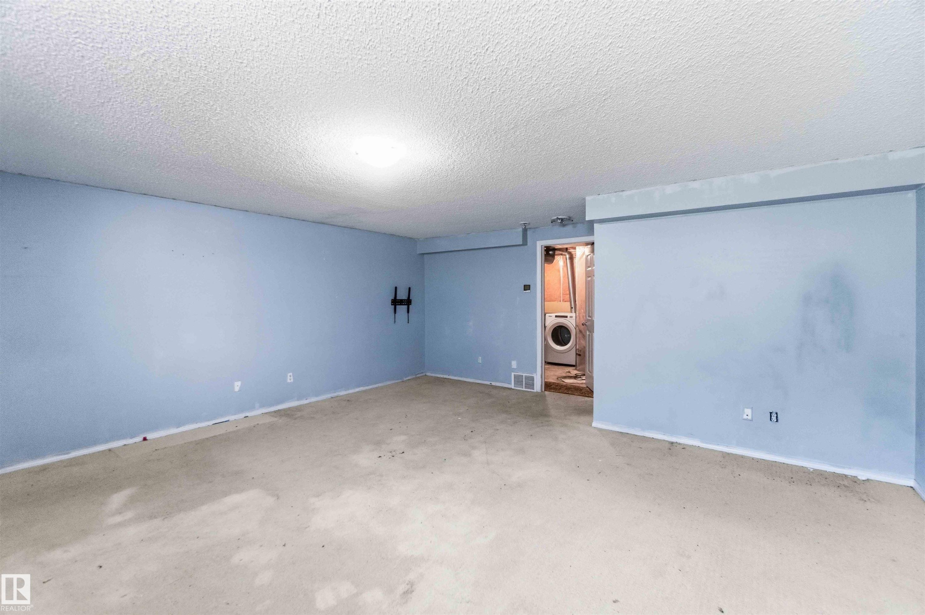 Spacious interior room featuring light blue painted walls, an exposed concrete floor, and a popcorn ceiling with an overhead light fixture - #64 120 Magrath Rd Nw, Edmonton, AB - Indoor Photo Showing Other Room