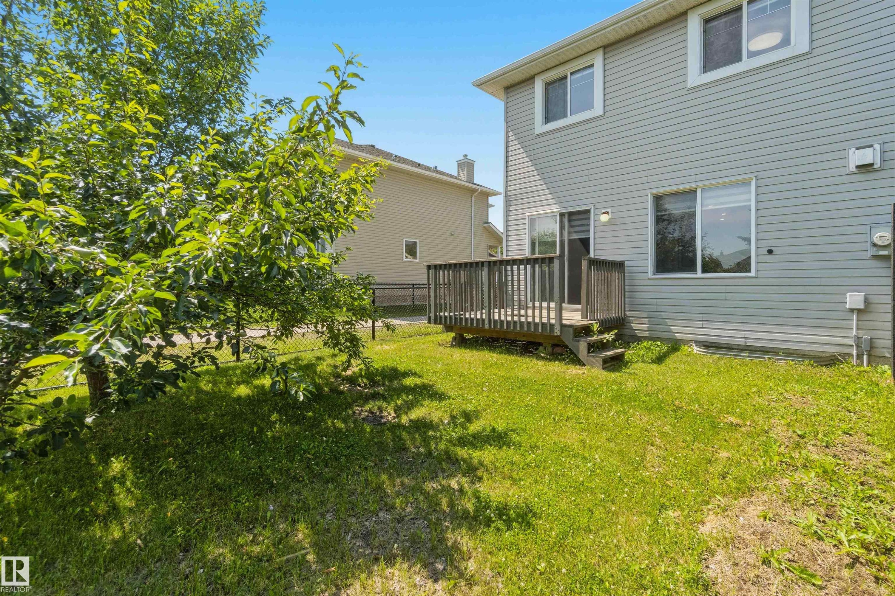 Expansive backyard featuring a wood deck with steps, a sliding glass door for outdoor access, and mature trees - #64 120 Magrath Rd Nw, Edmonton, AB - Outdoor