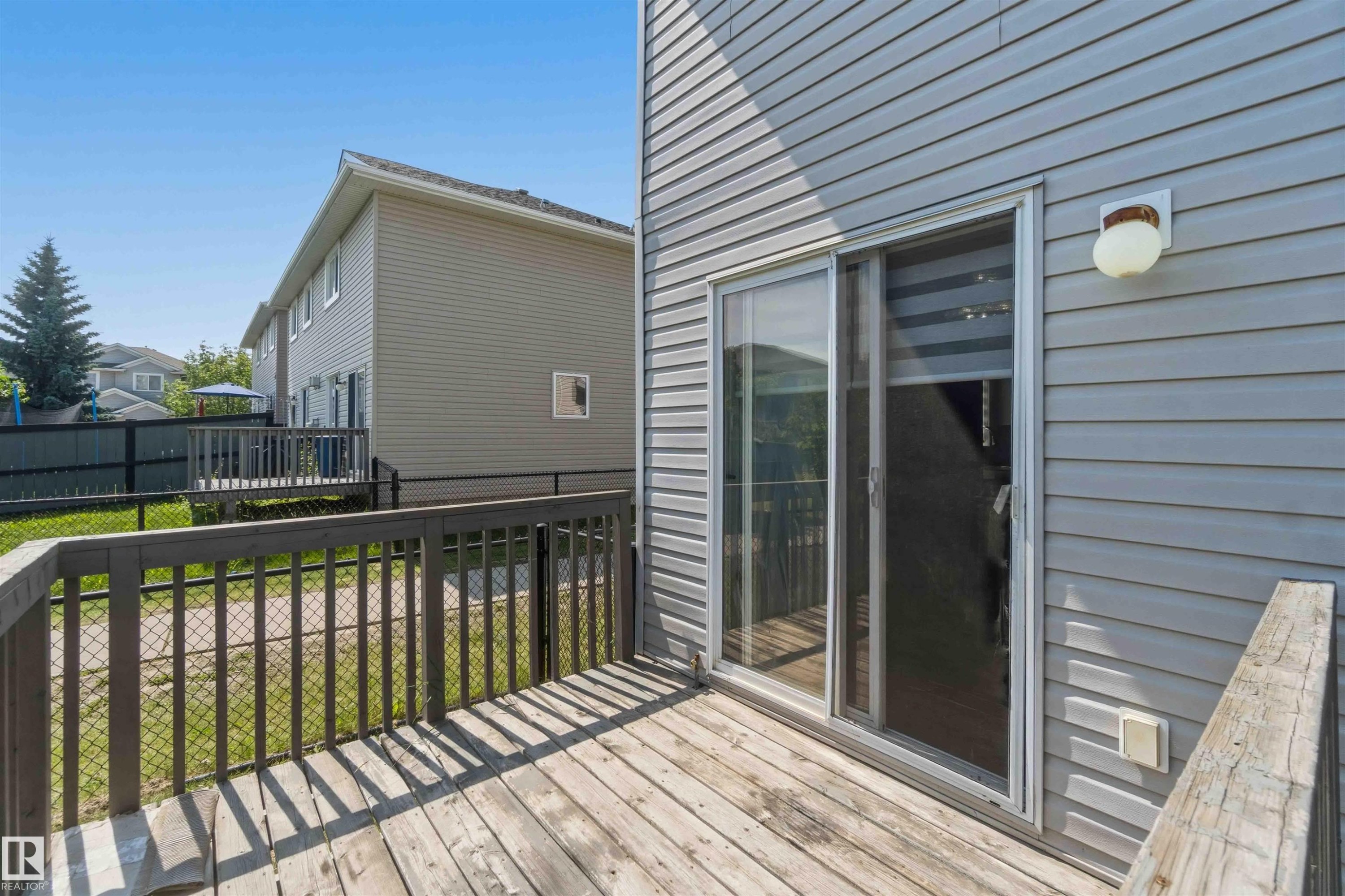 Outdoor wood deck featuring a sliding glass door entry, vinyl siding exterior, and a chain-link fence - #64 120 Magrath Rd Nw, Edmonton, AB - Outdoor With Deck Patio Veranda With Exterior