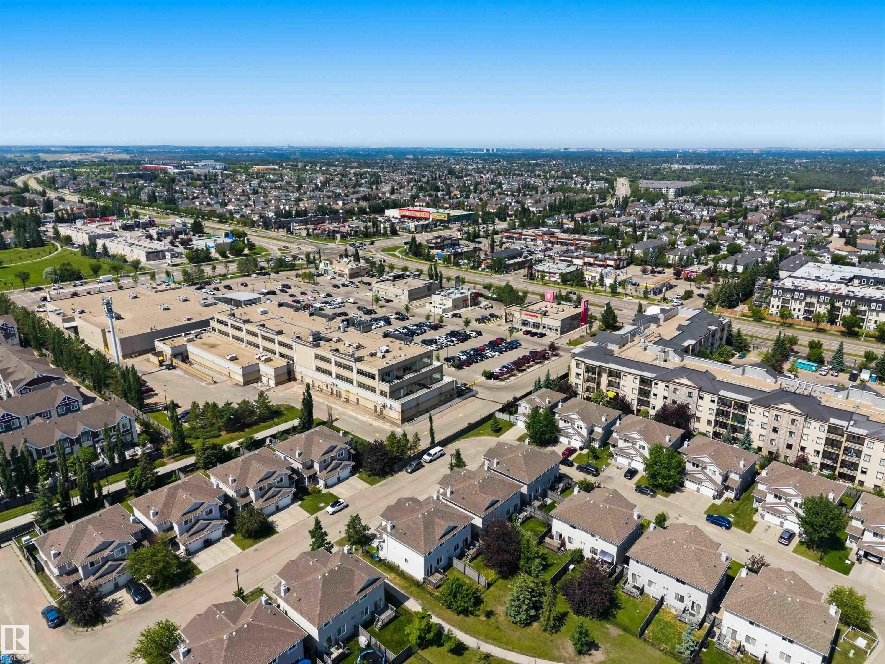 Expansive suburban landscape featuring residential homes with pitched roofs, a large commercial building with extensive parking, multi-story apartment buildings, and mature green spaces - #64 120 Magrath Rd Nw, Edmonton, AB - Outdoor With View