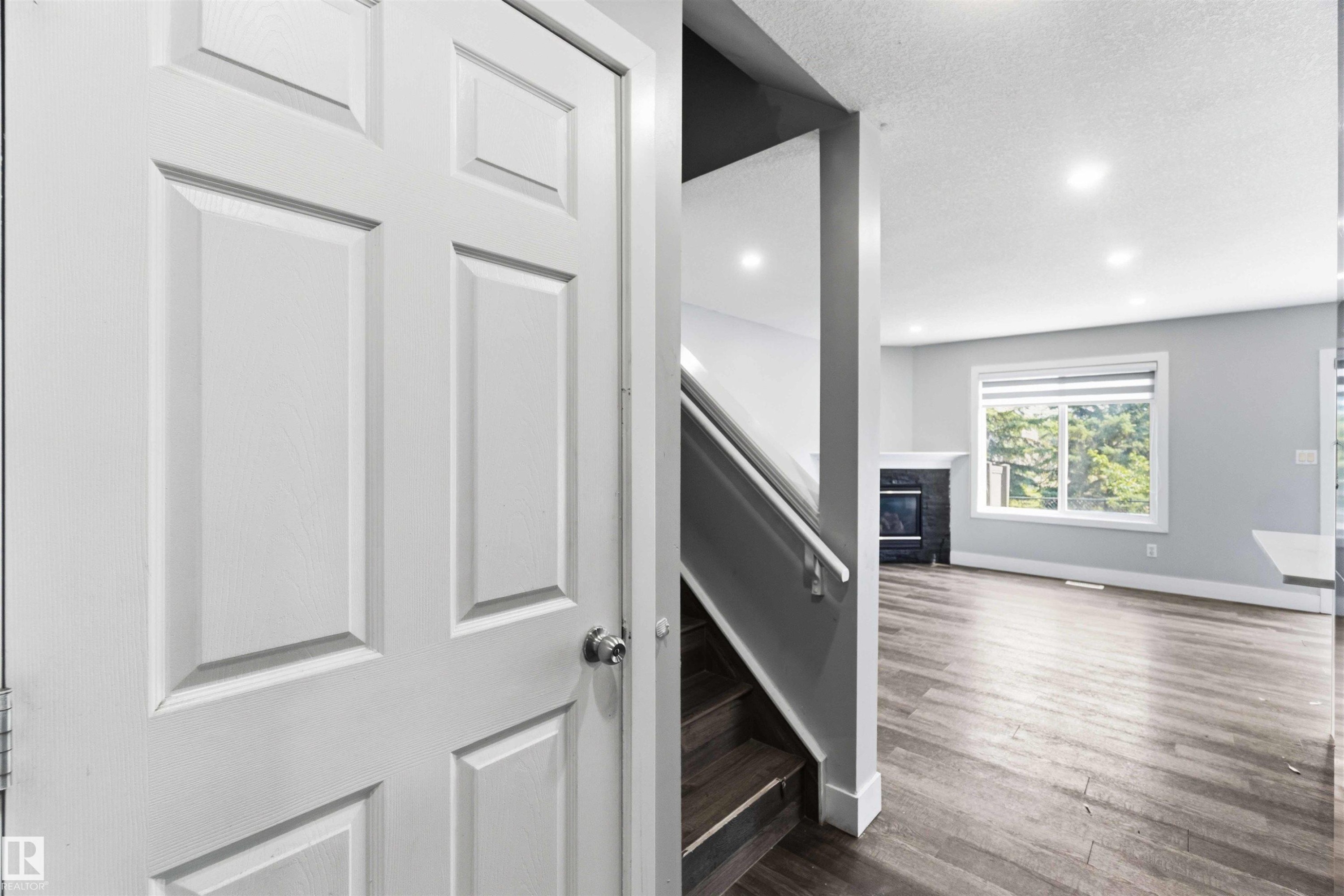 Four-panel interior door opening to a living area featuring wood-finish flooring, recessed lighting, and a window with horizontal blinds - #64 120 Magrath Rd Nw, Edmonton, AB - Indoor Photo Showing Other Room