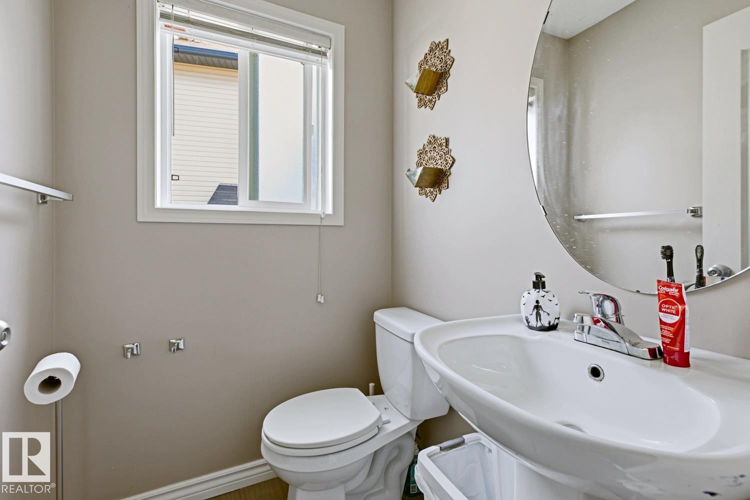 Bathroom featuring a single-pane window, wall-mounted oval mirror, and a white ceramic pedestal sink - 3724 163 Avenue Nw, Edmonton, AB - Indoor Photo Showing Bathroom