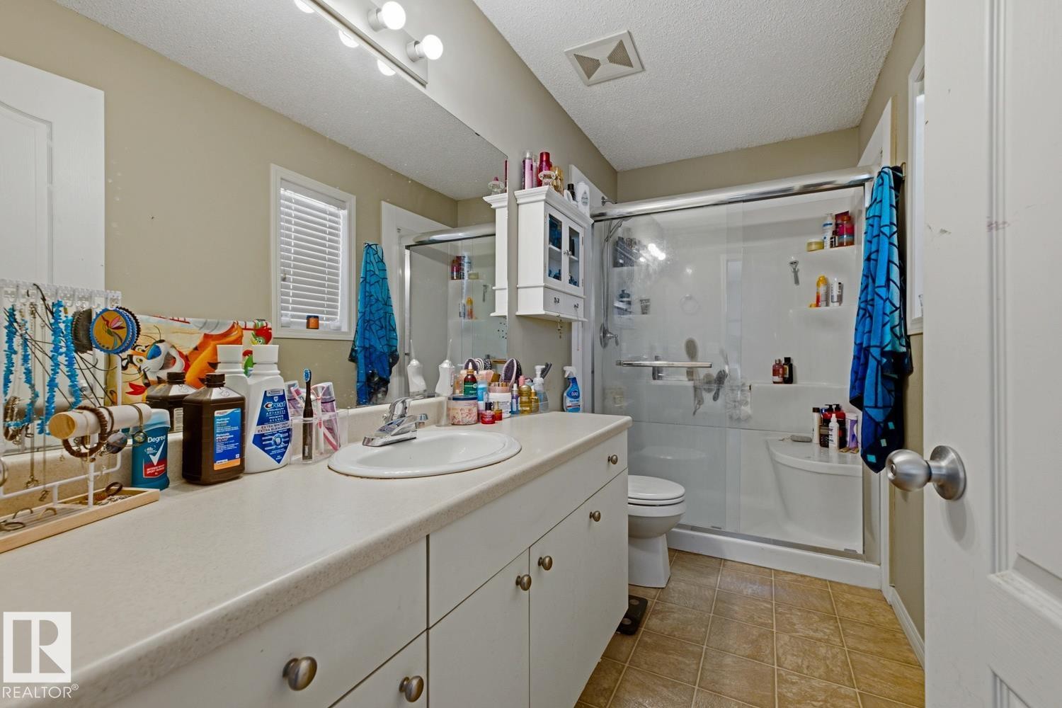 Bathroom featuring a single vanity with an integrated sink, a large mirror, a shower with a sliding glass door, and tiled flooring - 3724 163 Avenue Nw, Edmonton, AB - Indoor Photo Showing Bathroom
