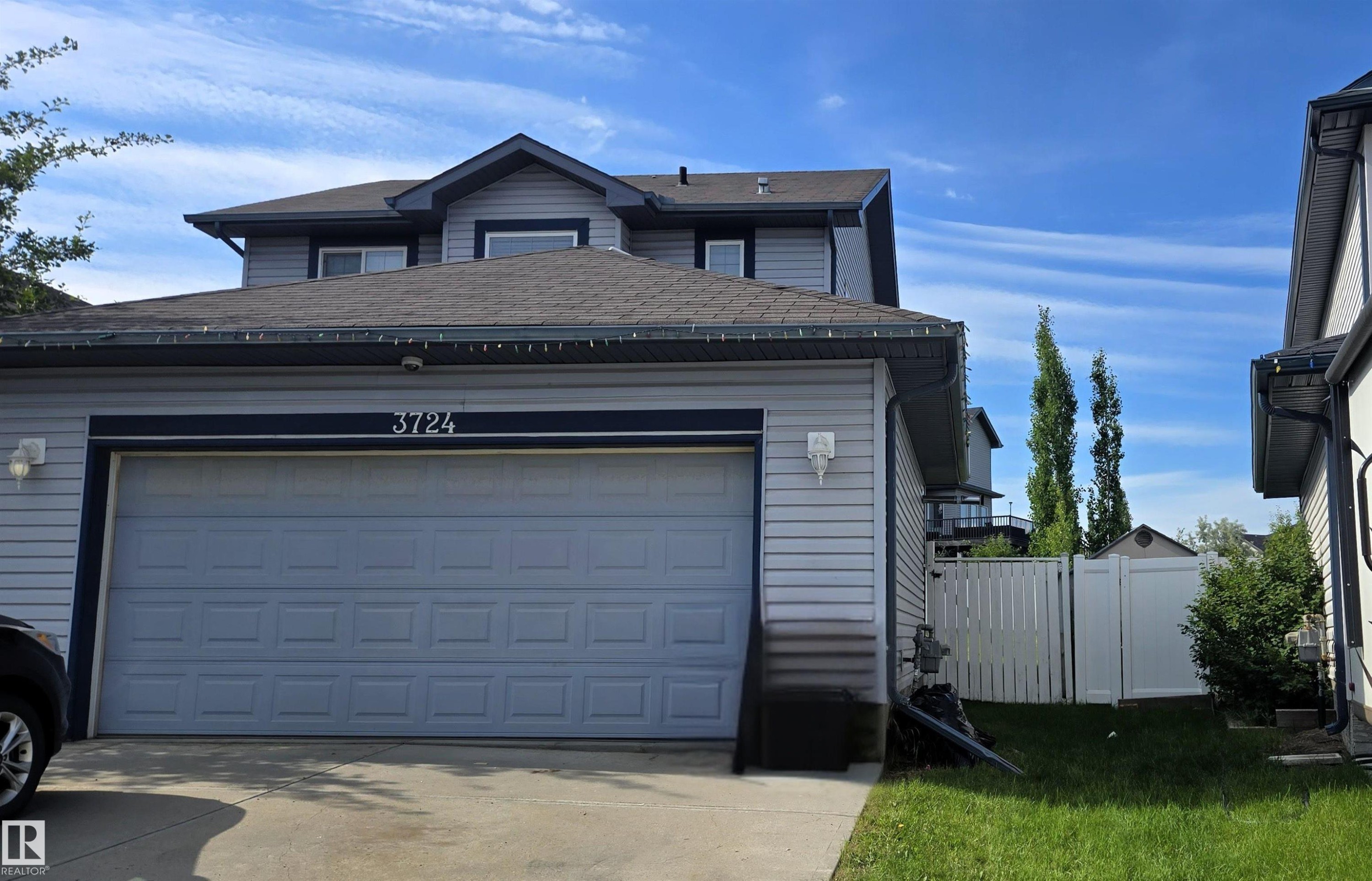 Two-story residence featuring light gray siding, a charcoal gray shingle roof, and a prominent two-car garage with a panel door - 3724 163 Avenue Nw, Edmonton, AB - Outdoor