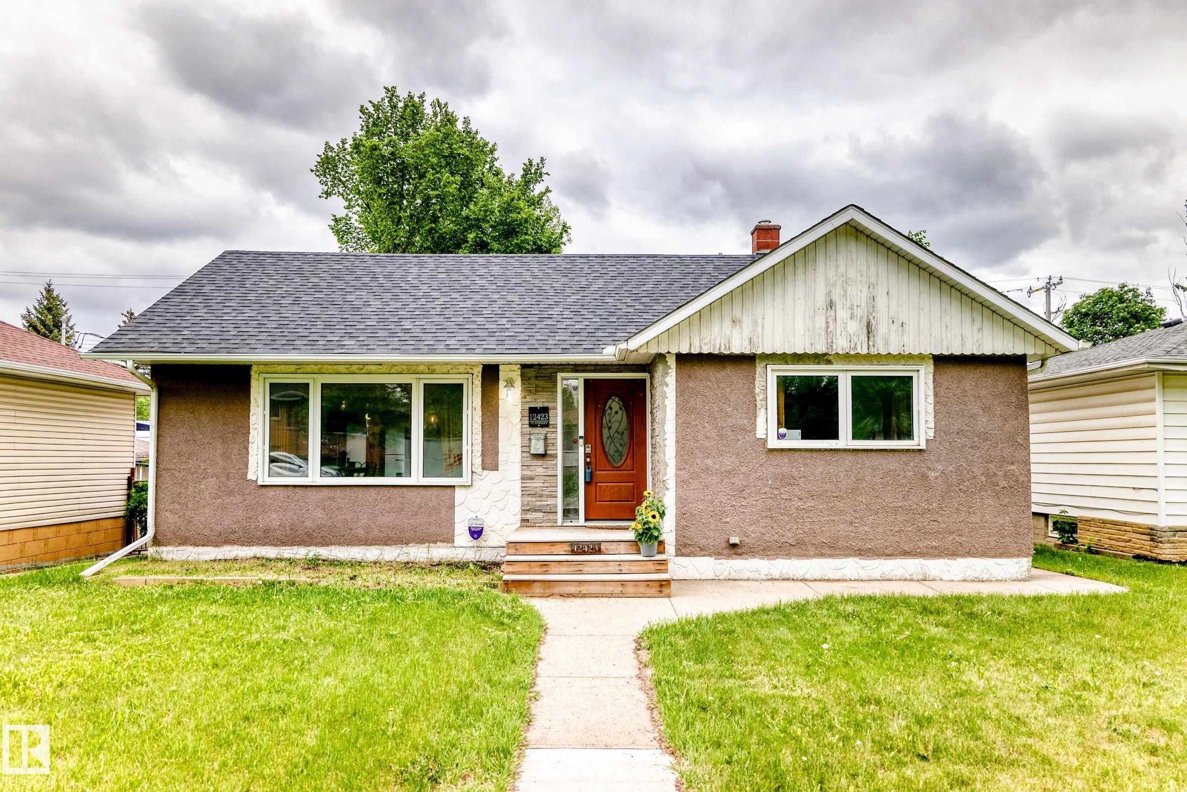 Bungalow-style residence featuring a textured stucco exterior, asphalt shingle roof, and a prominent red entry door with oval glass insert - 12423 75 Street, Edmonton, AB
