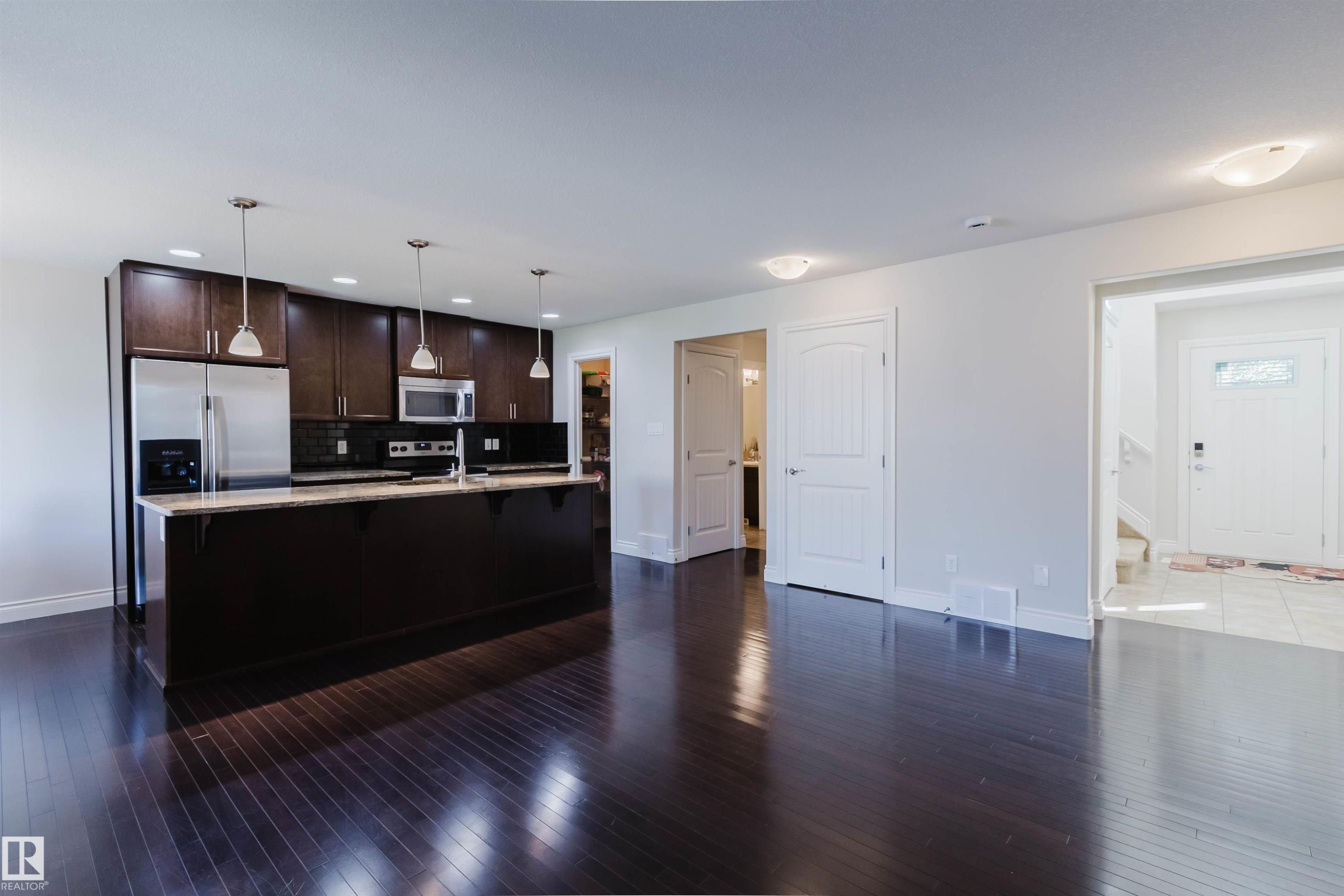 Open-concept kitchen featuring dark wood cabinetry, stainless steel appliances, a central island with pendant lighting, and dark wood-finish flooring - 17348 6 Avenue Sw, Edmonton, AB - Indoor Photo Showing Kitchen