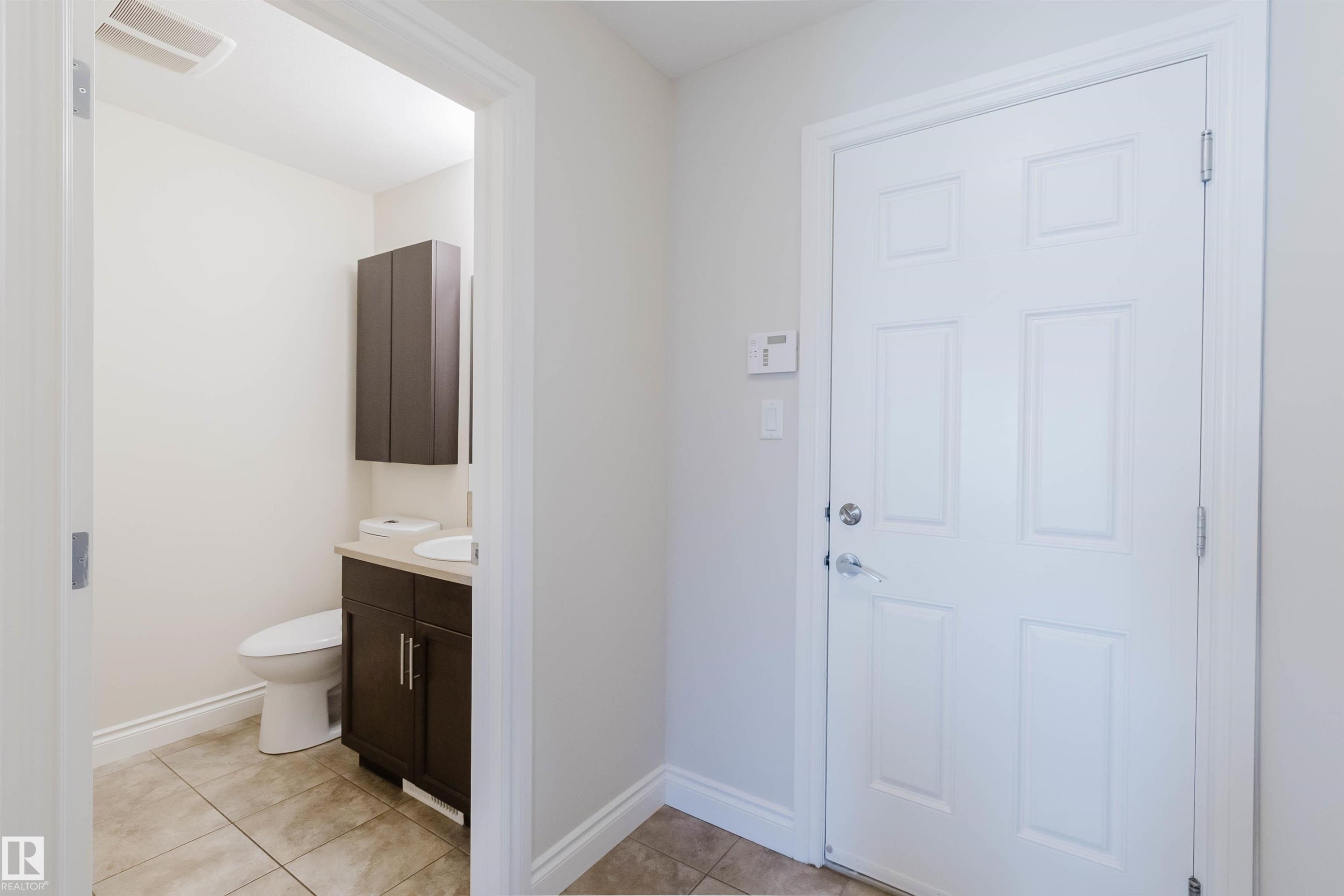 Powder room featuring a dark wood-finish vanity with a white countertop and an integrated sink, a matching wall-mounted cabinet, and large-format tile flooring - 17348 6 Avenue Sw, Edmonton, AB - Indoor Photo Showing Bathroom