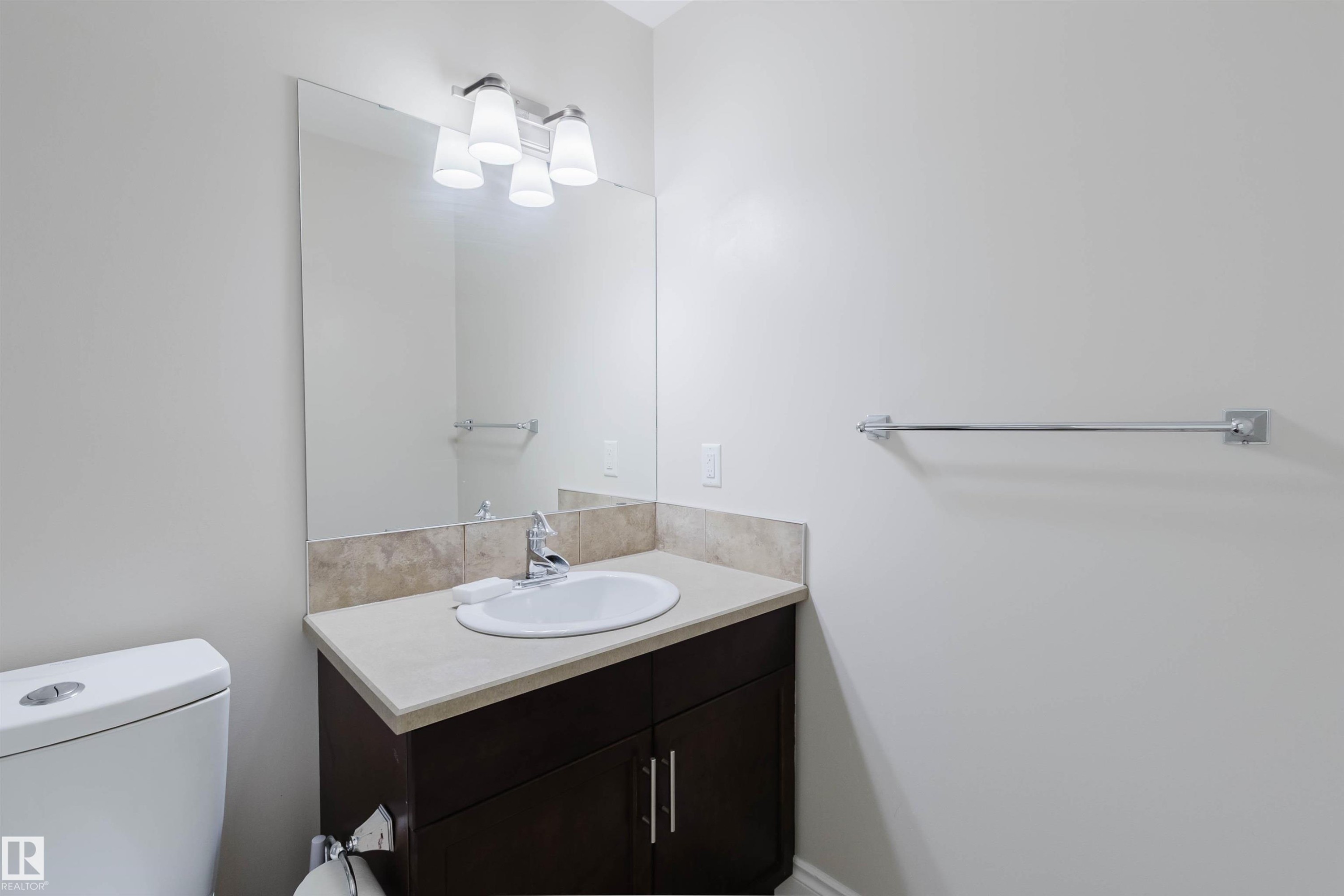 Bathroom featuring a vanity with a dark wood-finish cabinet, light countertop, and a white undermount sink - 17348 6 Avenue Sw, Edmonton, AB - Indoor Photo Showing Bathroom