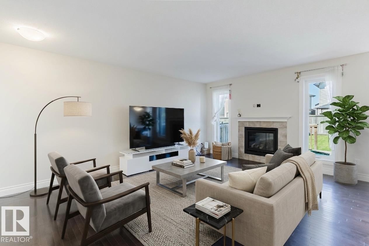 Bright living area featuring dark wood-finish flooring, a contemporary fireplace with a stone-tile surround and white mantel, and multiple windows - 17348 6 Avenue Sw, Edmonton, AB - Indoor Photo Showing Living Room With Fireplace