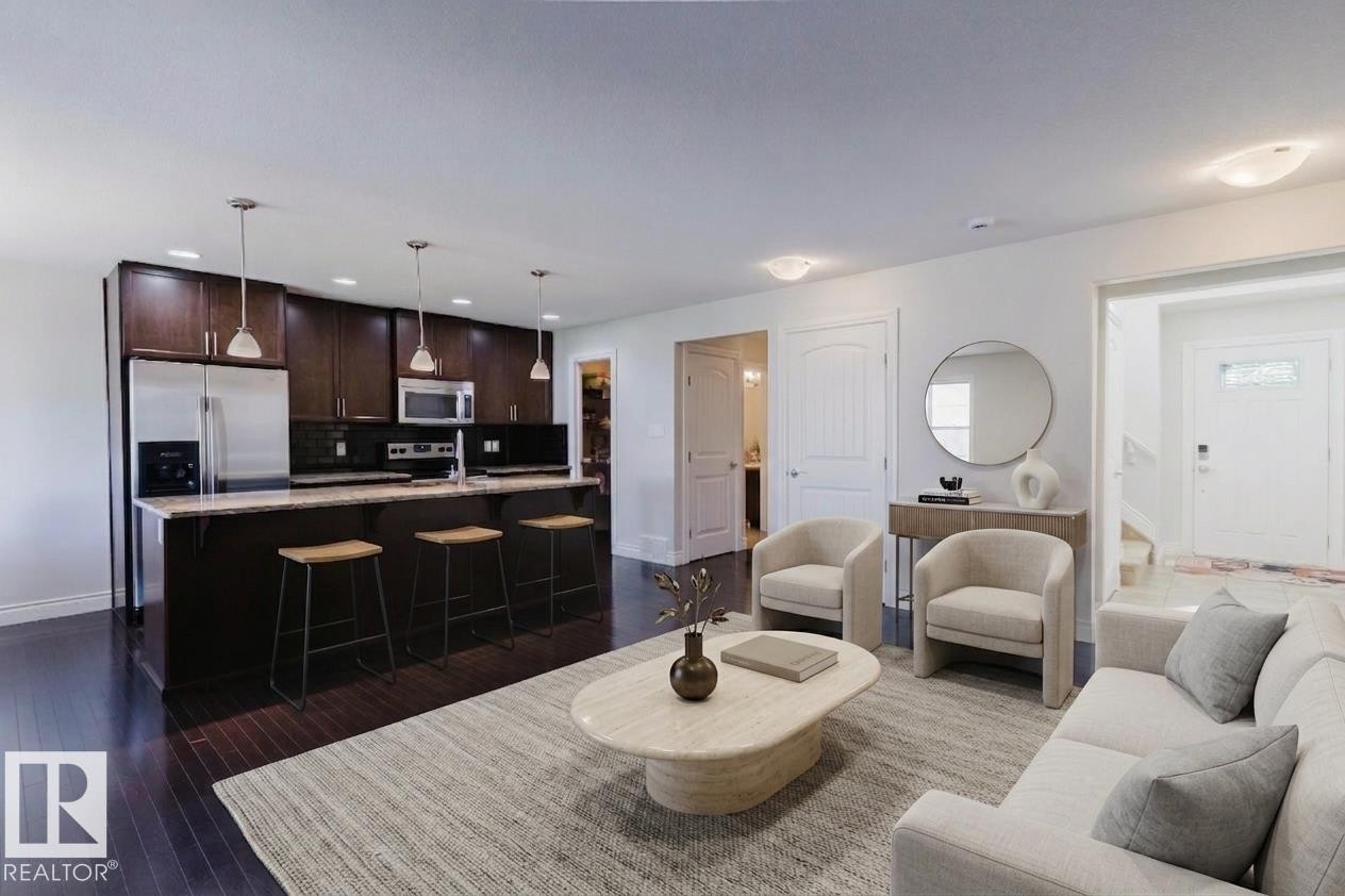 Open-concept living space featuring rich dark wood-finish flooring, a kitchen island with pendant lighting, dark cabinetry, and integrated stainless steel appliances - 17348 6 Avenue Sw, Edmonton, AB - Indoor